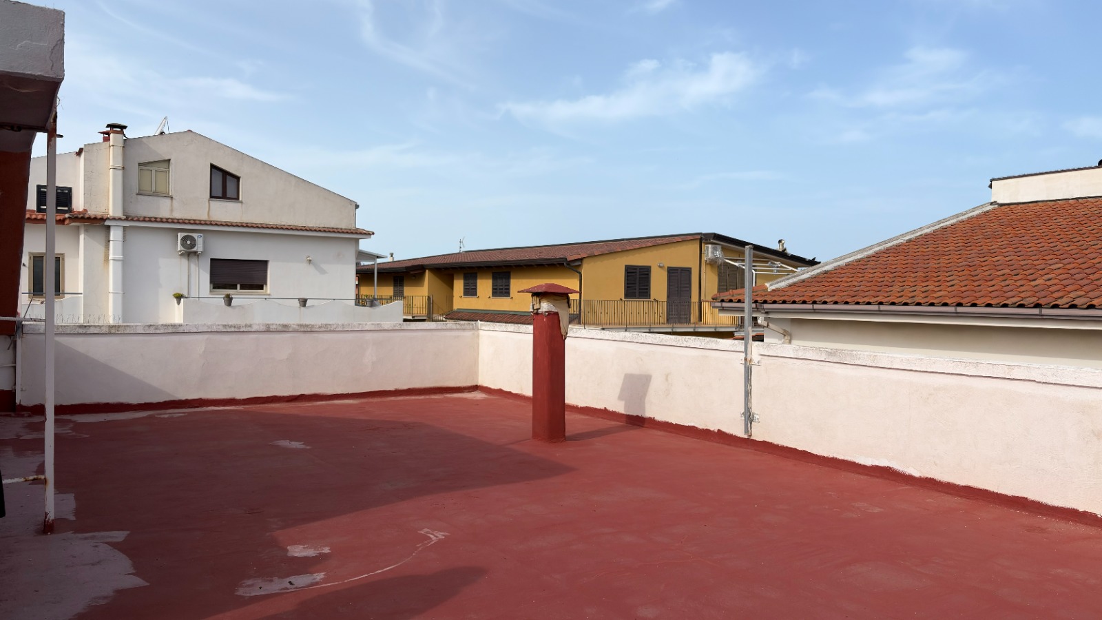 Ampio terrazzo all'aperto con vista urbana, superficie pavimentata in rosso, ideale per relax e socializzazione, in zona residenziale tranquilla vicino a servizi e negozi.