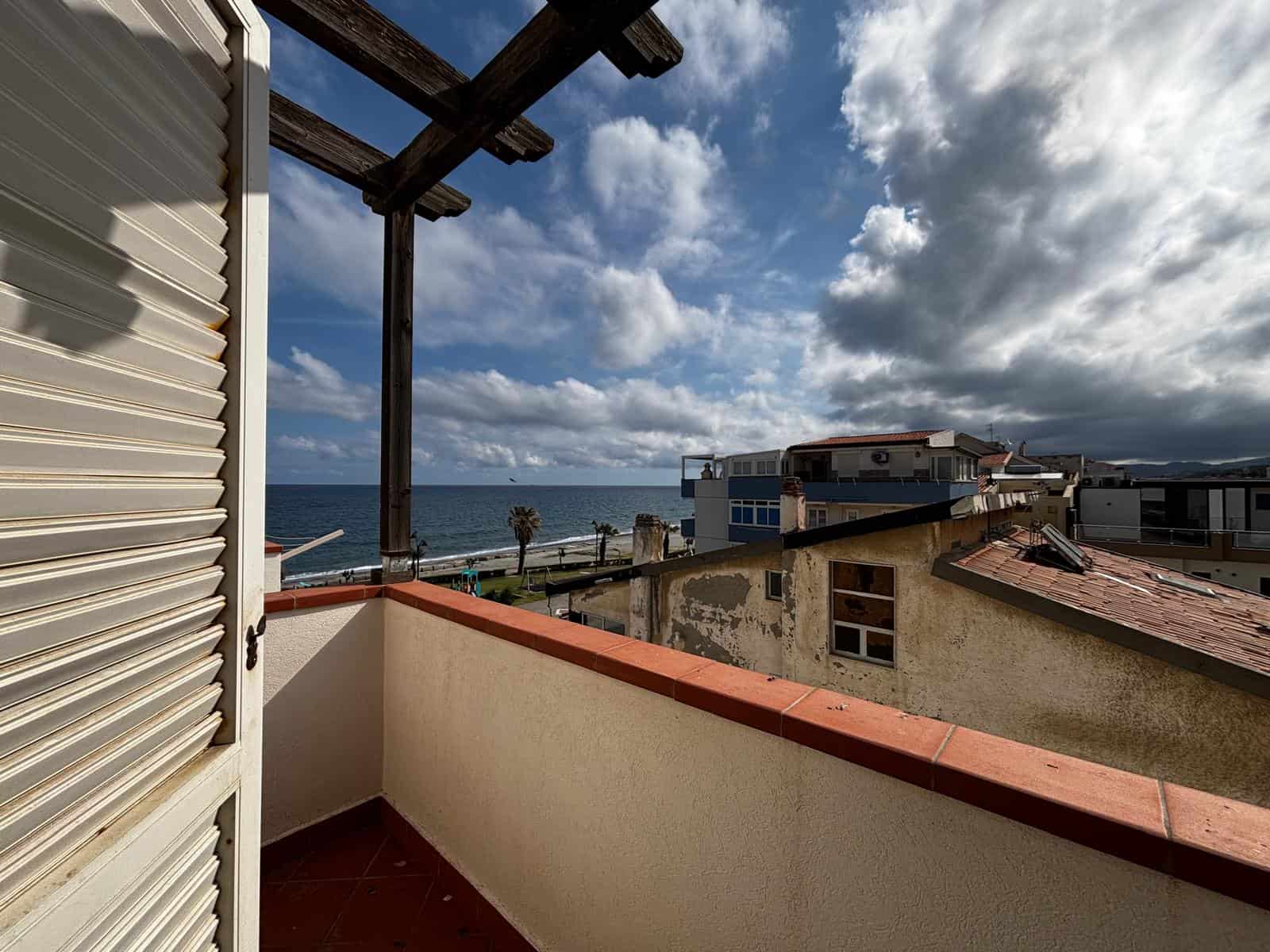Ampio balcone con vista mare, cielo nuvoloso e edifici residenziali, ideale per relax e godersi il panorama costiero.