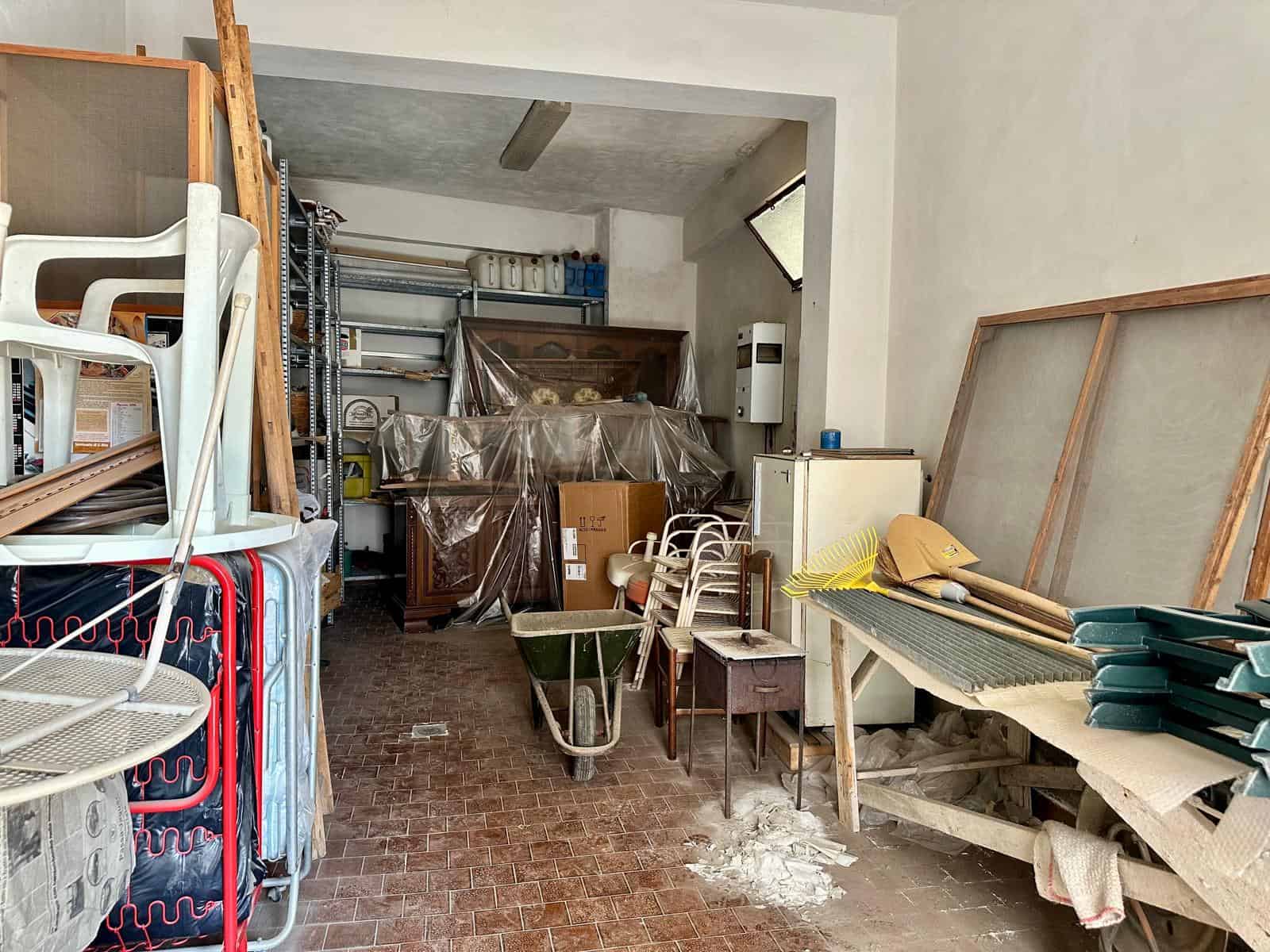 Spazio di magazzino o deposito con scaffali, mobili e materiali vari, ambiente industriale con pavimento in piastrelle e pareti bianche.