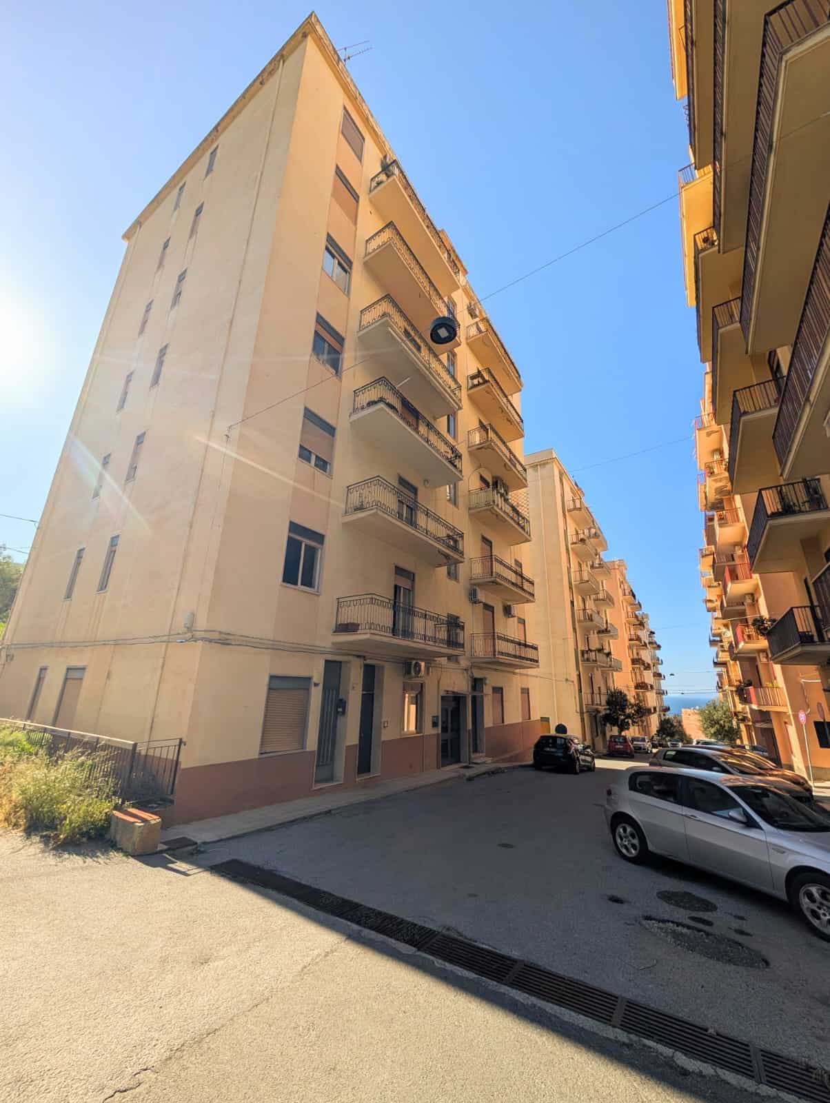 Balcone di un appartamento in un edificio residenziale con parcheggio esterno, cielo azzurro e luce solare naturale, in un contesto urbano a NextCasa, soluzione immobiliare a Napoli.
