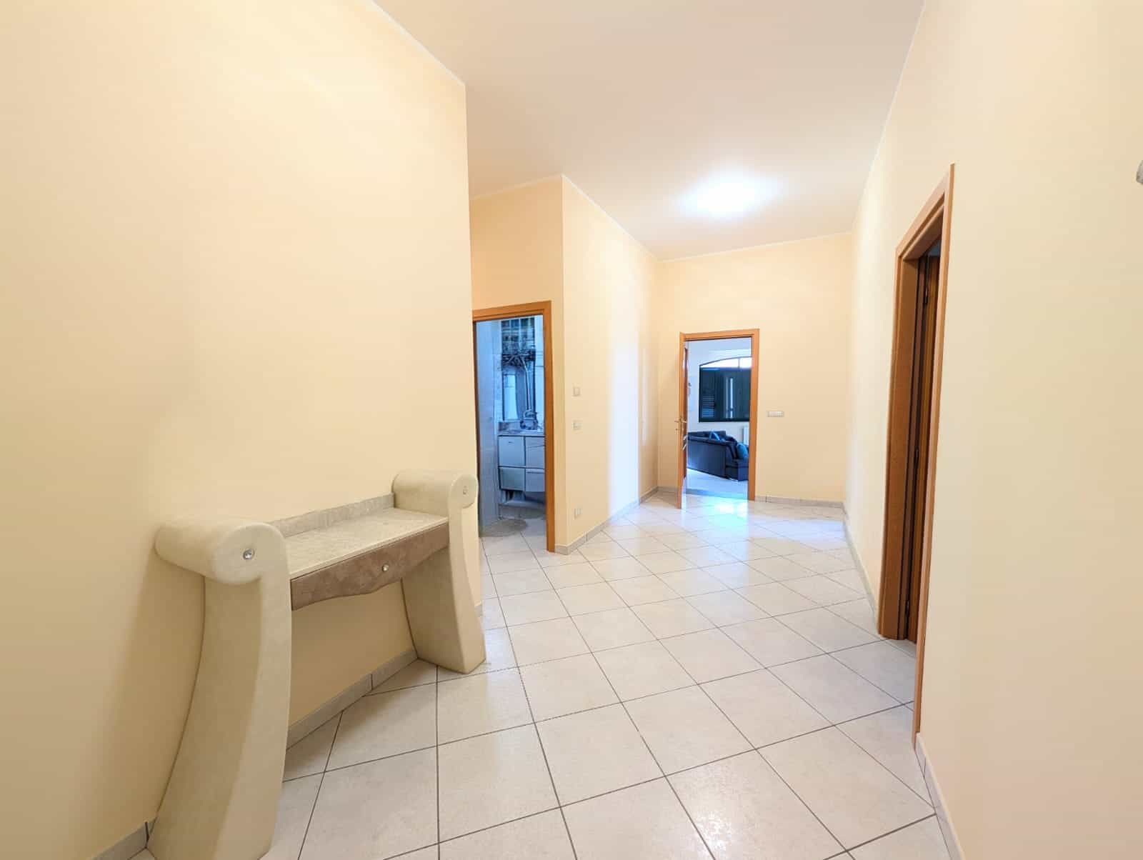 Porte interne in legno e pareti color crema in un appartamento luminoso e spazioso, con pavimento in piastrelle bianche. Ideale per chi cerca soluzioni di arredamento eleganti e funzionali.