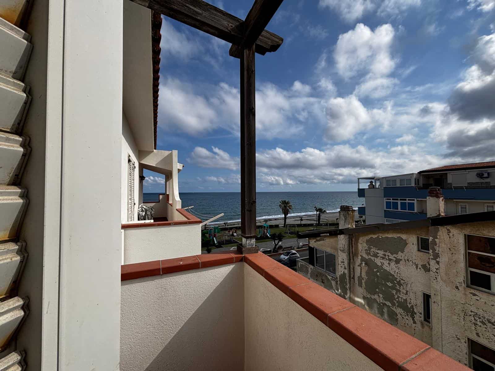 VISTA MARE DAL BALCONE DI UN APPARTAMENTO IN AFFITTO O VENDITA, CON BALCONE IN PRIMA LINEA, CIELO PARZIALMENTE NUVOLOSO E OCEANO IN SFONDO, IN UN CONTESTO URBANO MEDITERRANEO.