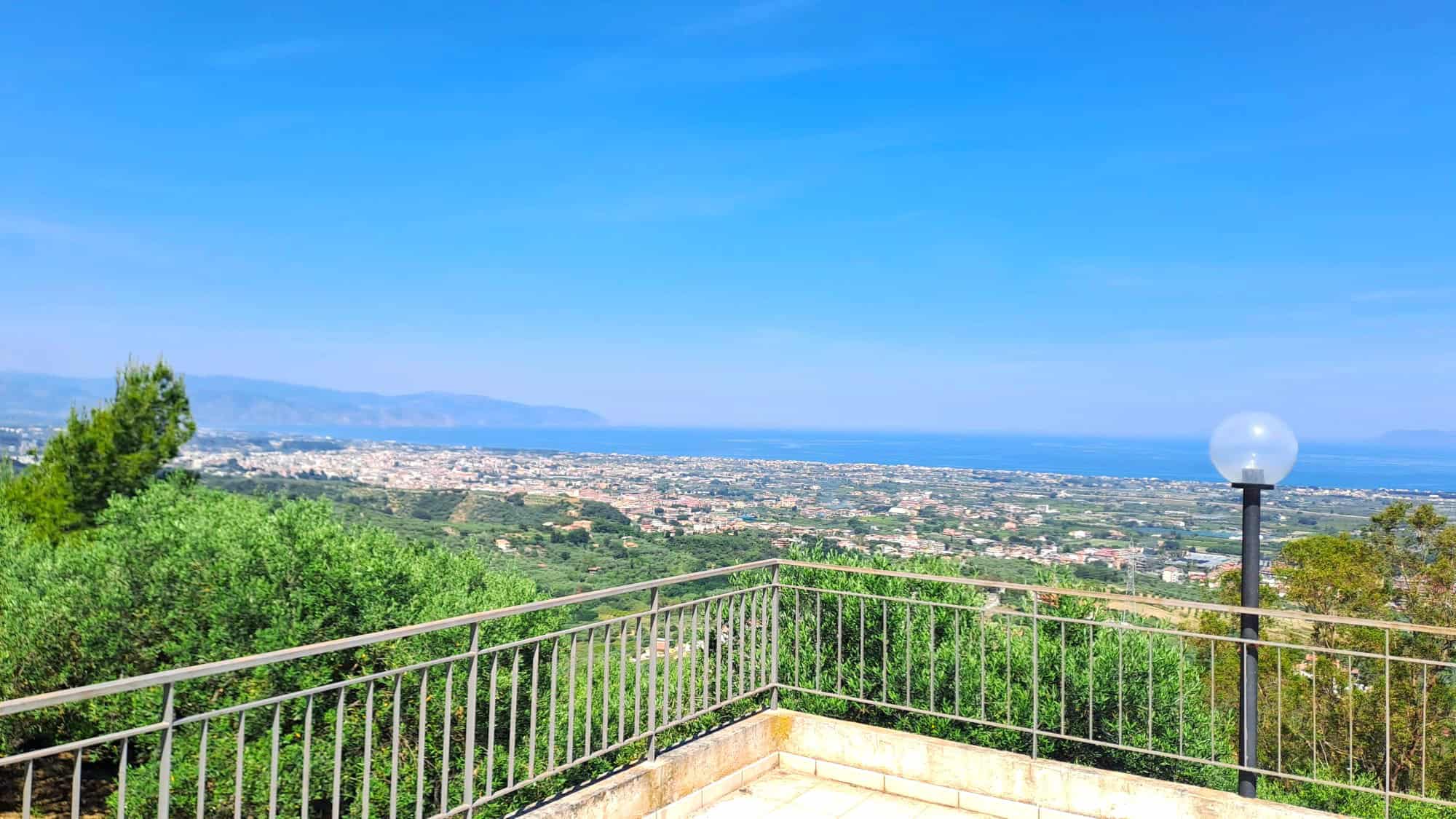 Vista panoramica sulla campagna e il mare dal terrazzo di una casa in vendita a NextCasa, con ringhiera in metallo e lampione, in un ambiente tranquillo e suggestivo.