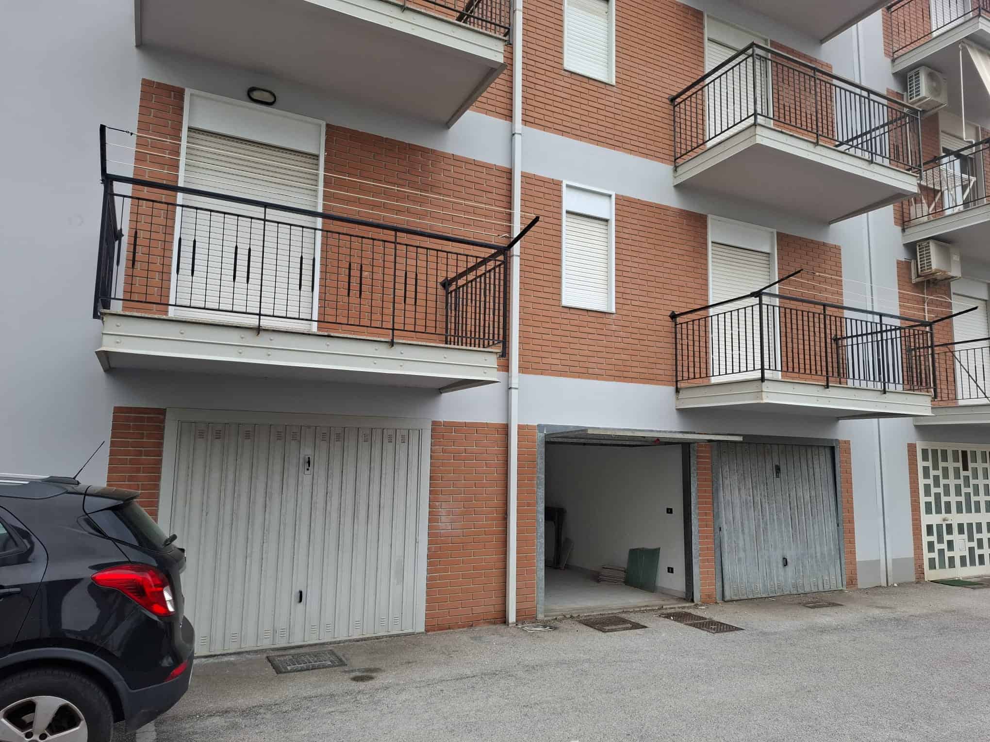 Un edificio residenziale con garage al piano terra, balconi con ringhiere in metallo e pareti in mattoni rossi, situato in un'area urbana.