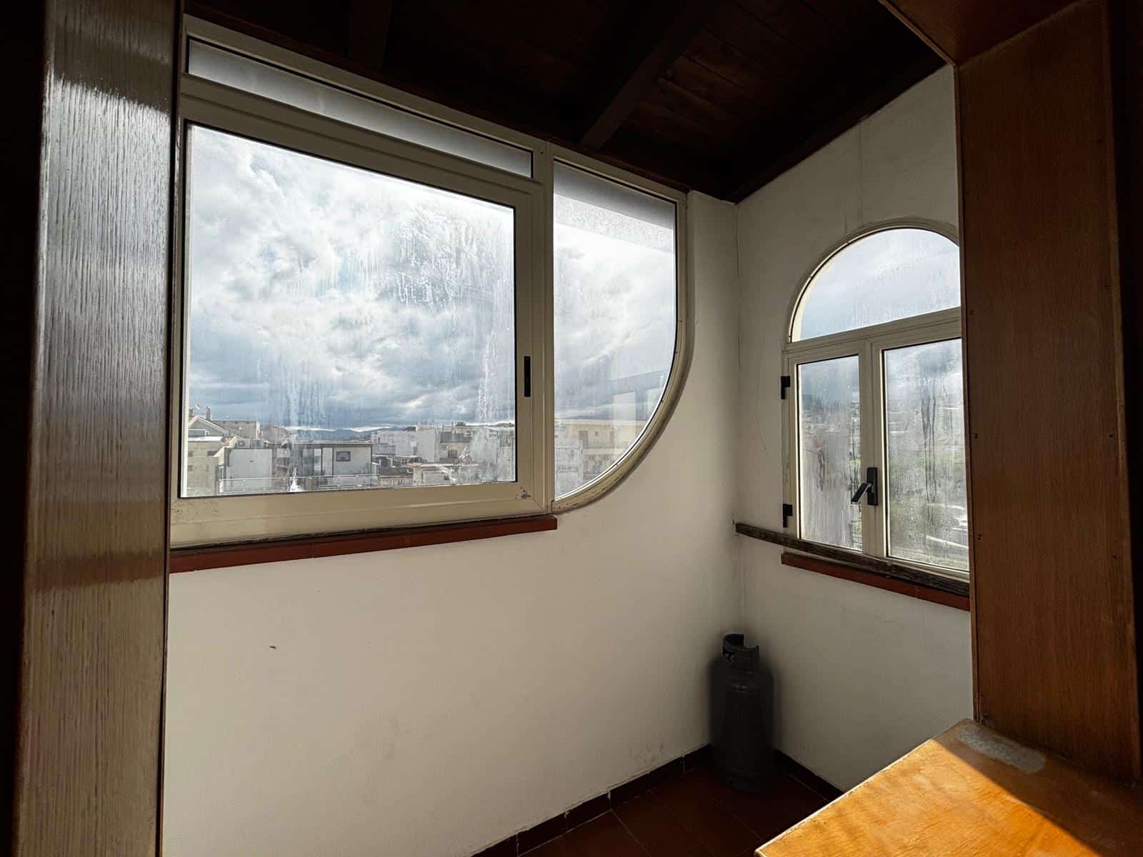 Ampio balcone con grandi finestre e vista sulla città, ideale per godersi momenti di relax e luce naturale. Perfetto per ambienti residenziali moderni e luminosi, con dettagli in legno e design funzio.
