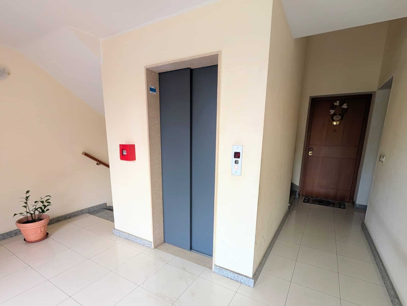 Ascensore condominio moderno con pareti beige e pavimento in piastrelle chiare, ingresso principale e corridoio interno, ambiente luminoso e accogliente.