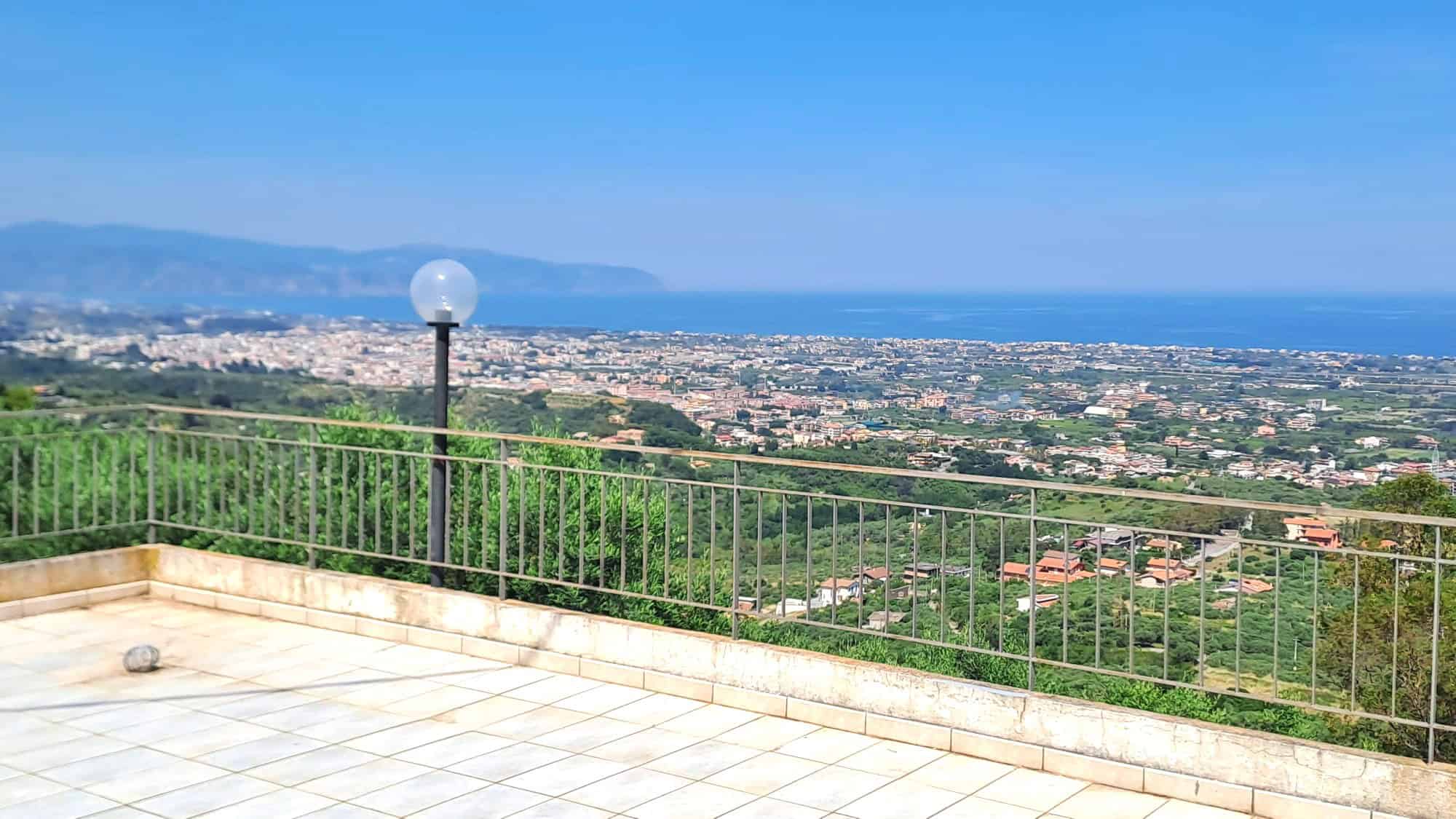 Vista panoramica sulla costa e sulla città dal terrazzo di una casa con ringhiera in metallo, in un'area verdeggiante e tranquilla, ideale per relax e momenti all'aperto.