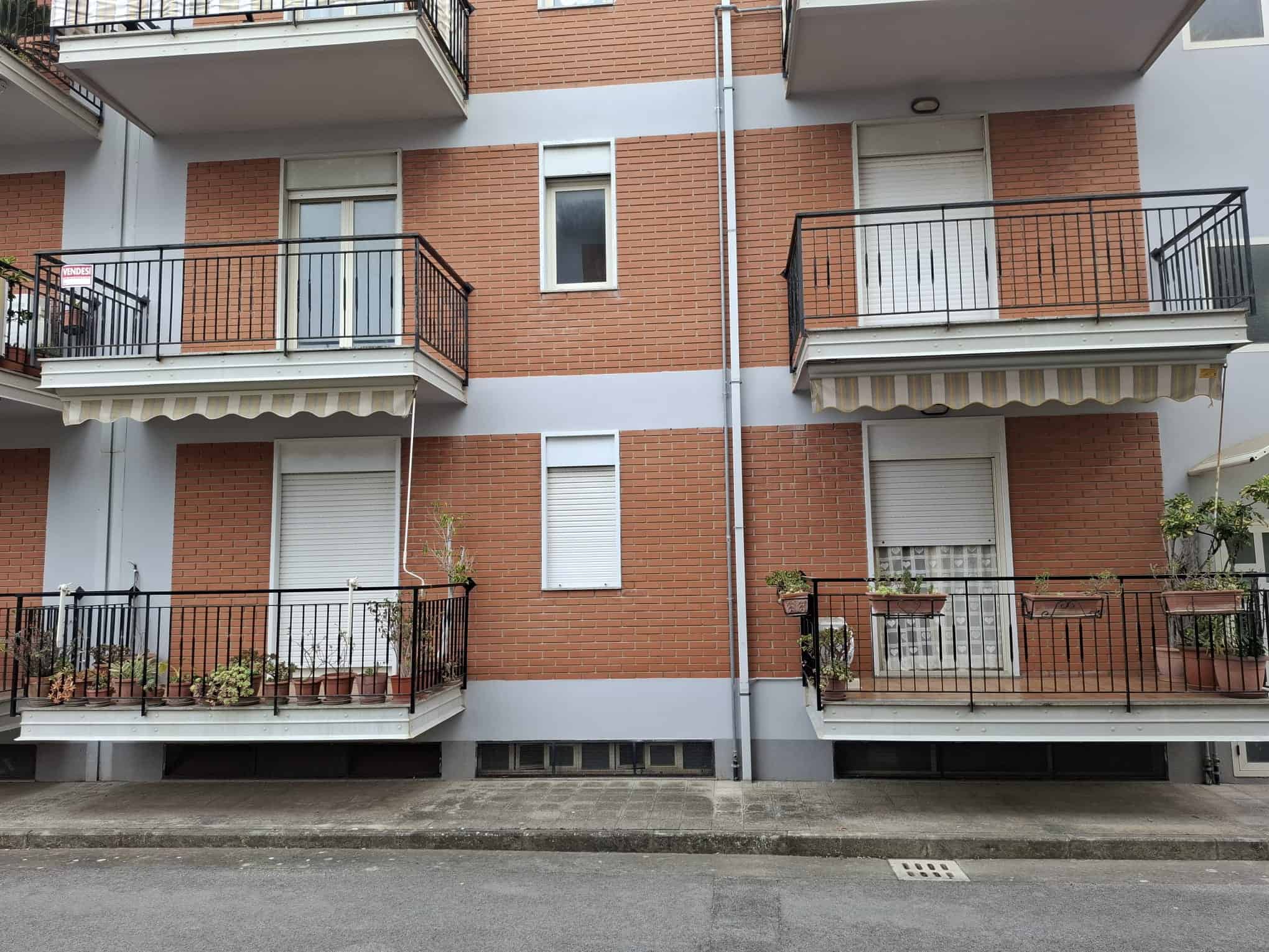 Appartamento con balconi e piante, facciata in mattoni rossi e dettagli in bianco, in un complesso residenziale moderno.
