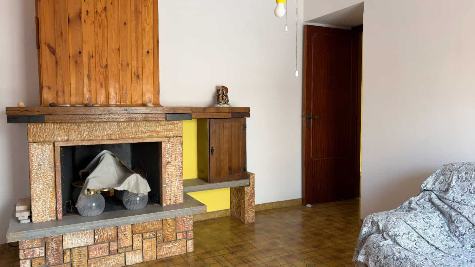 Camino in pietra e mattoni in un soggiorno accogliente con pareti bianche e pavimento in legno, arredato con divano e mobili in stile rustico, ideale per ambienti caldi e invitanti.