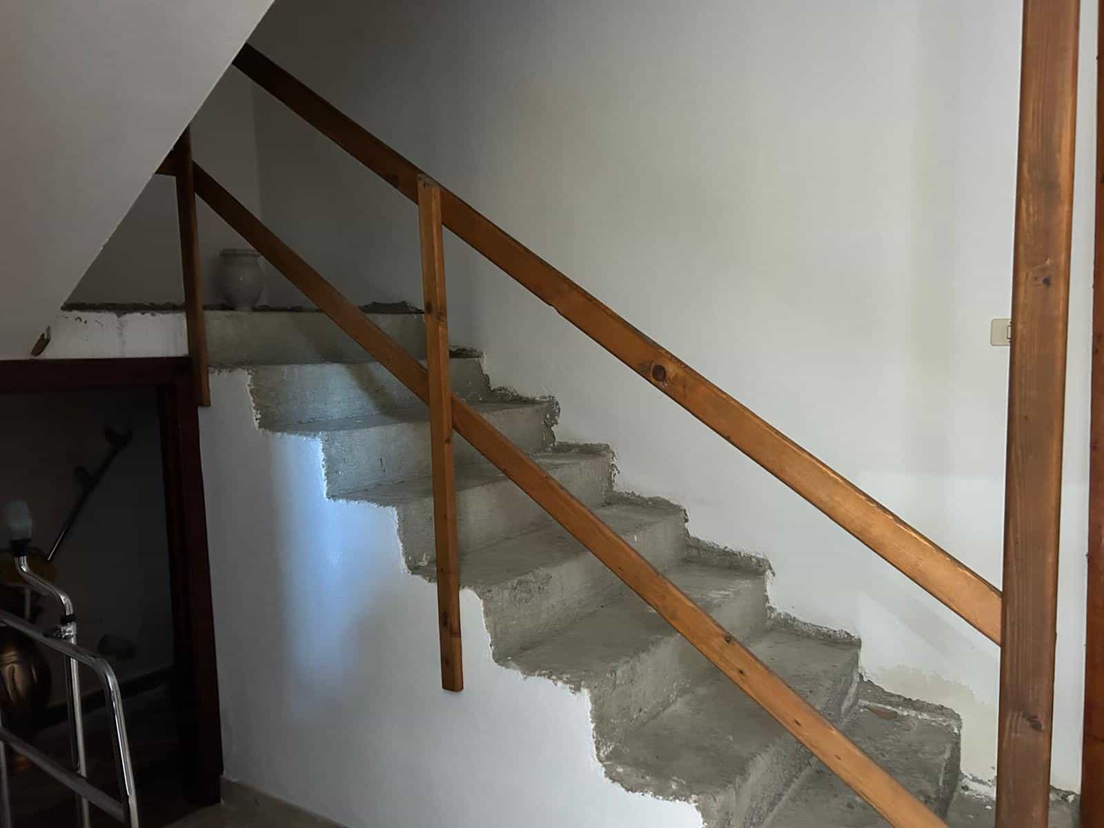Scale interna in fase di ristrutturazione con gradini in cemento e ringhiera in legno, ideale per progetti di ristrutturazione di case e appartamenti. Soluzione funzionale e moderna per ambienti abita.