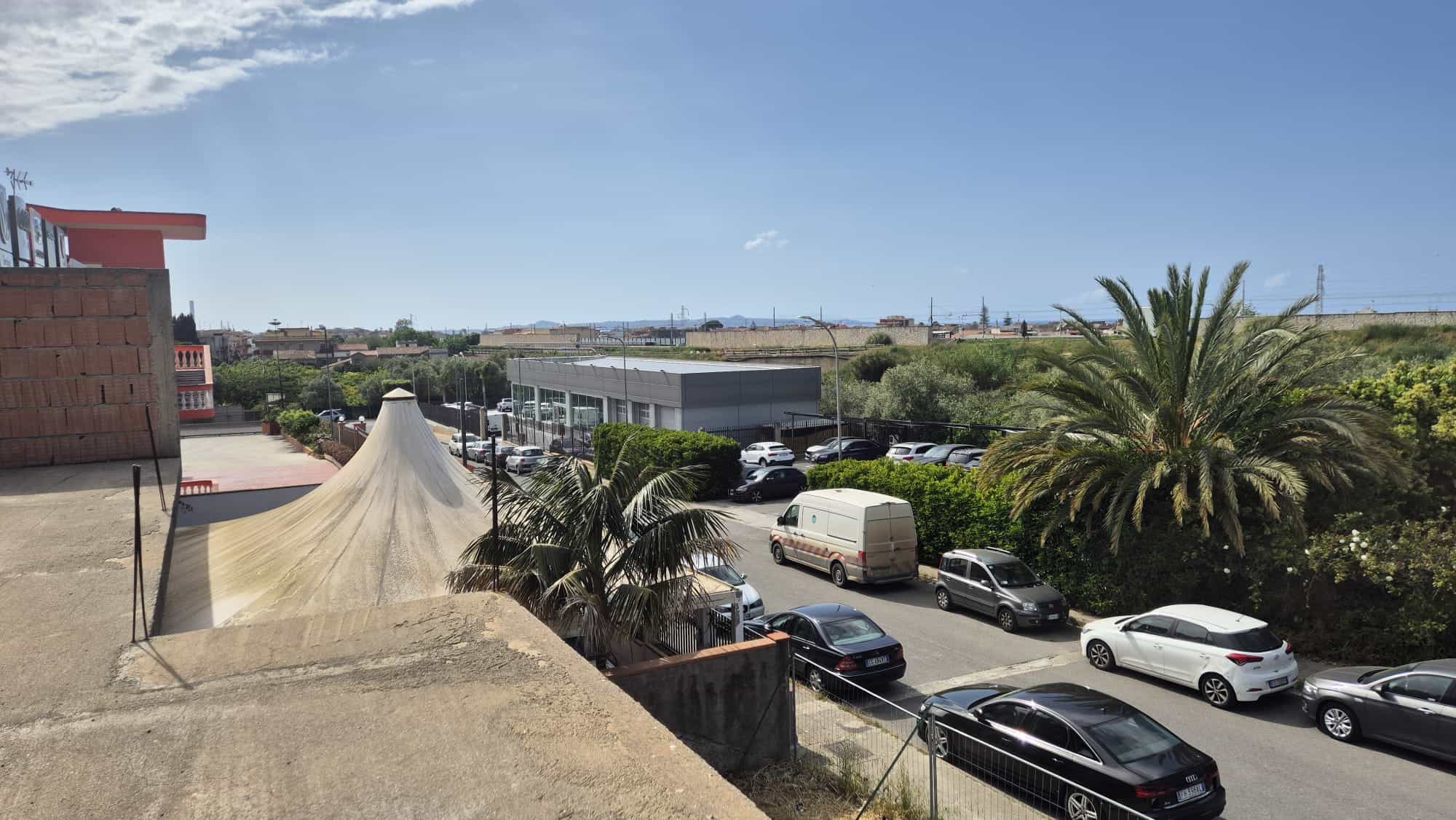 Ampio parcheggio esterno con auto parcheggiate, palme e vista panoramica sulla campagna e il cielo azzurro, ideale per residenze o attività commerciali in zona tranquilla e ben collegata.
