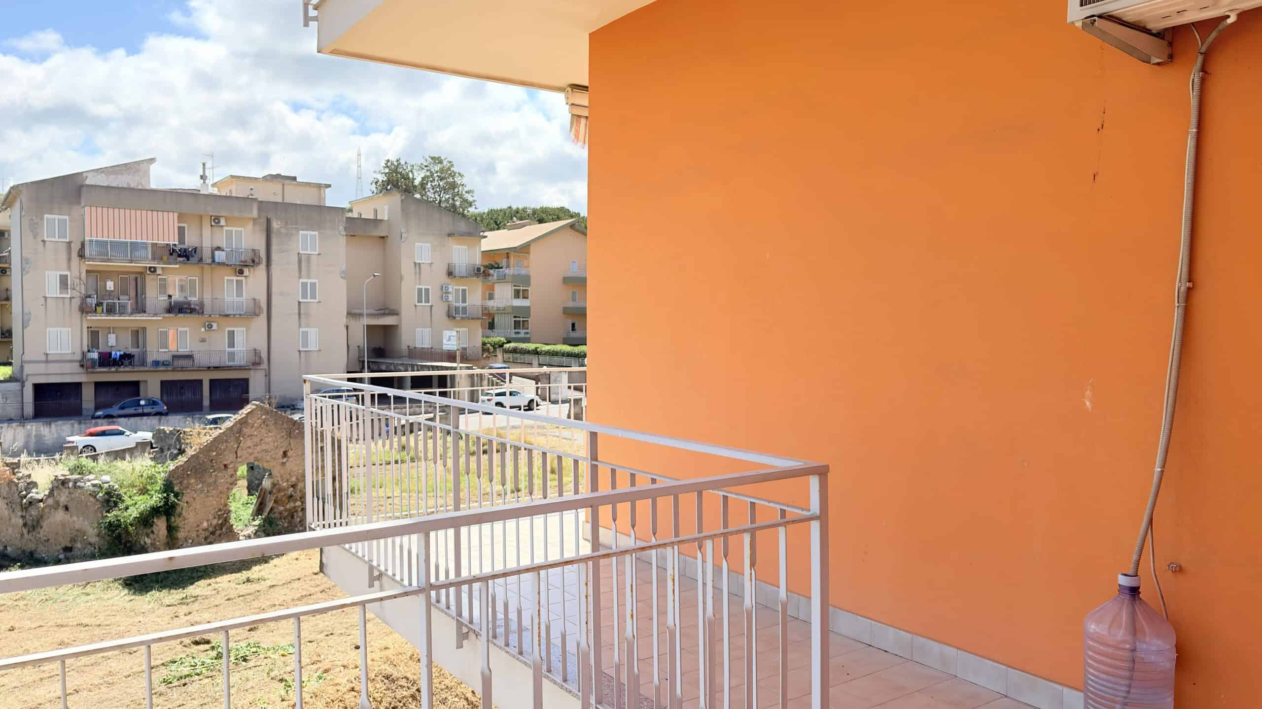 Ampio balcone con ringhiera bianca, vista su complesso residenziale con edifici moderni e cortile verde, in una giornata soleggiata.