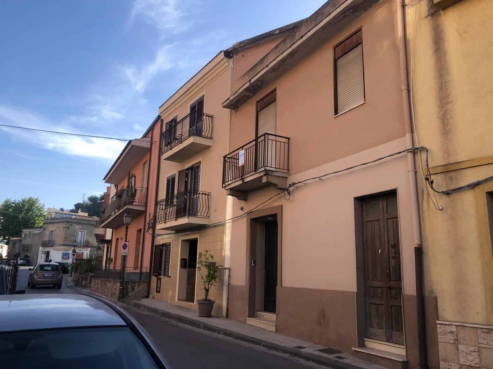 Vicolo con case residenziali in stile italiano, facciata colorata e balconi in ferro battuto, strada tranquilla con auto parcheggiate, atmosfera autentica e pittoresca.
