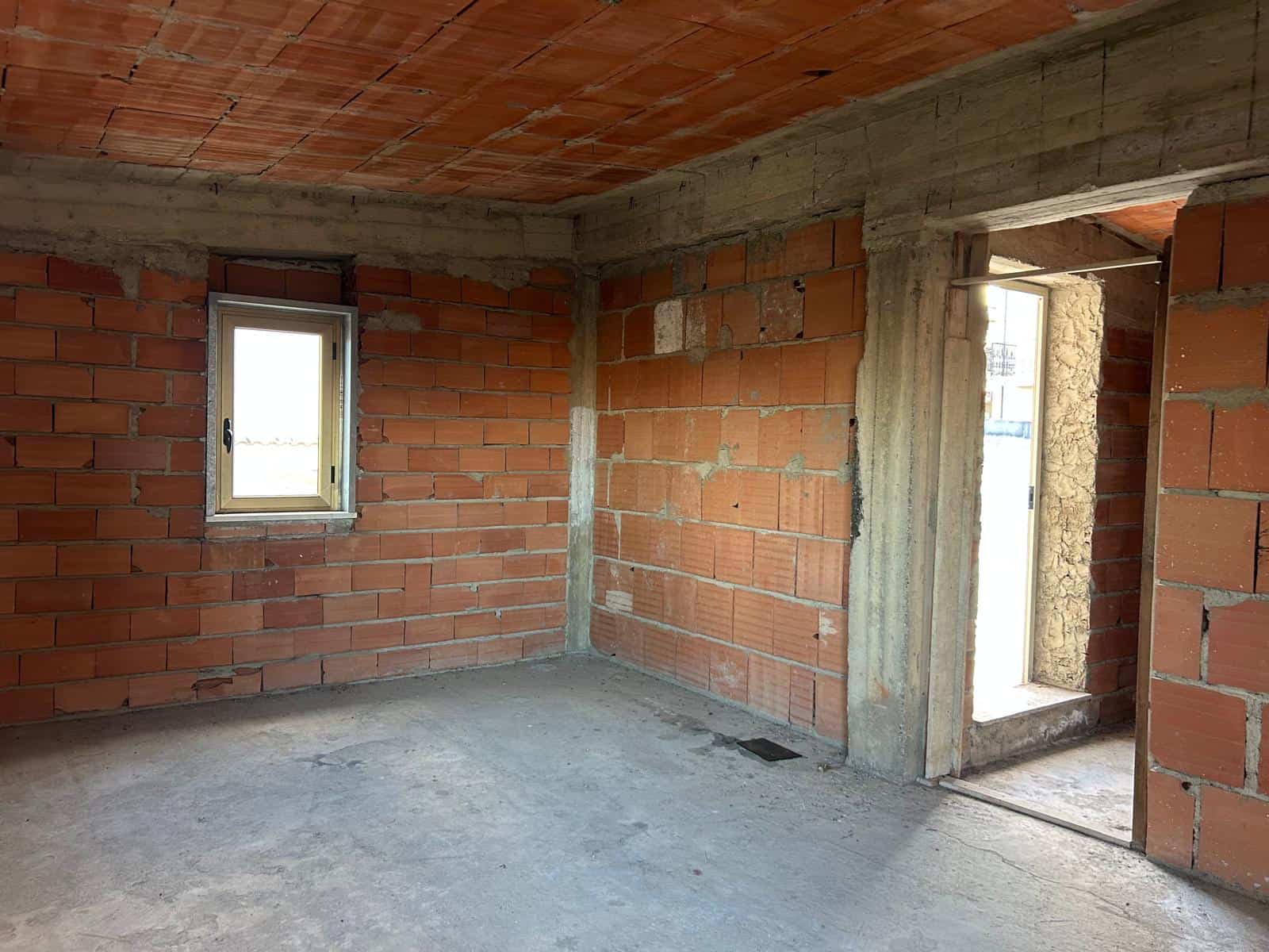 Interno di una casa in costruzione con pareti in mattoni e finestre senza finiture, pronto per essere completato.