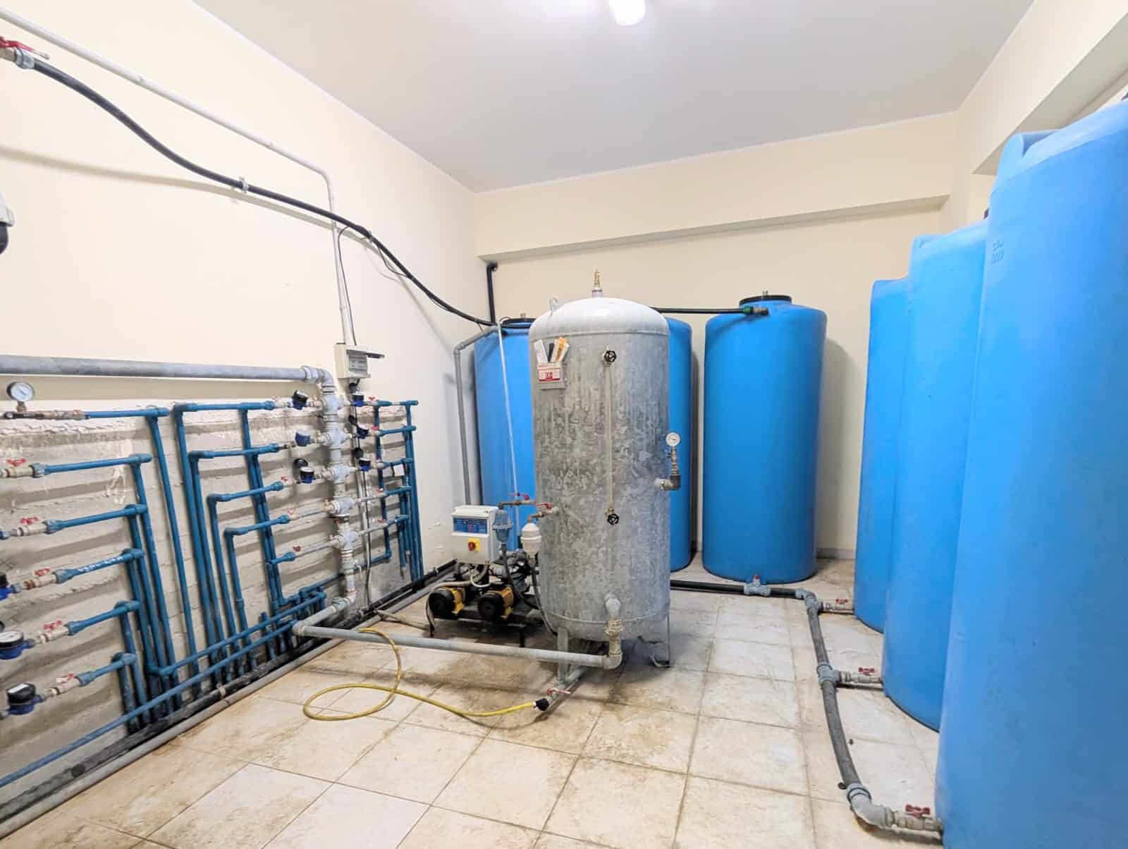 Acqua calda e sistemi di filtrazione in un locale tecnico domestico con serbatoi e tubature blu.