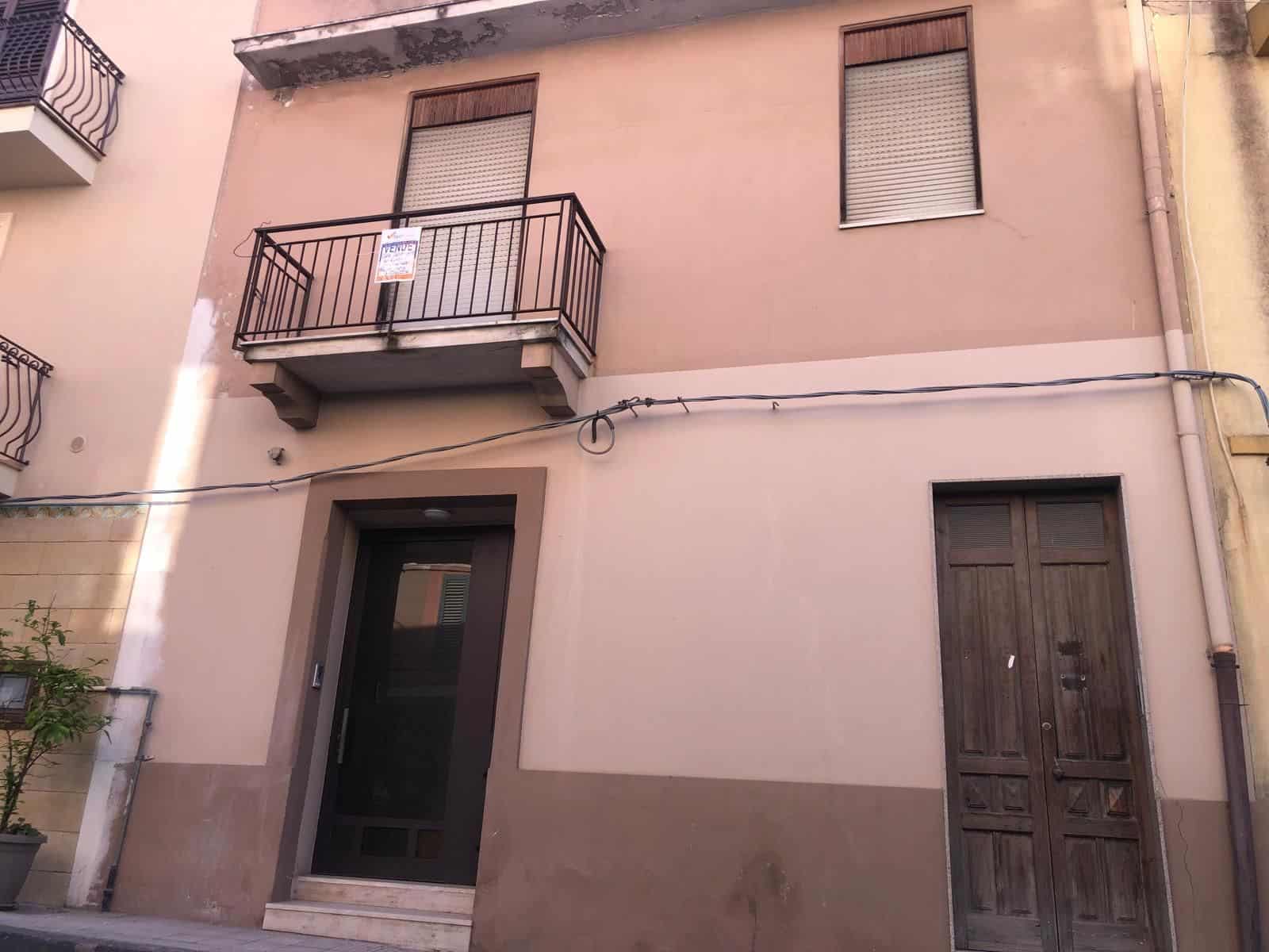 Un balcone e una porta d'ingresso di una casa in un edificio residenziale, con pareti di colore rosa e dettagli in legno, in un contesto urbano italiano.