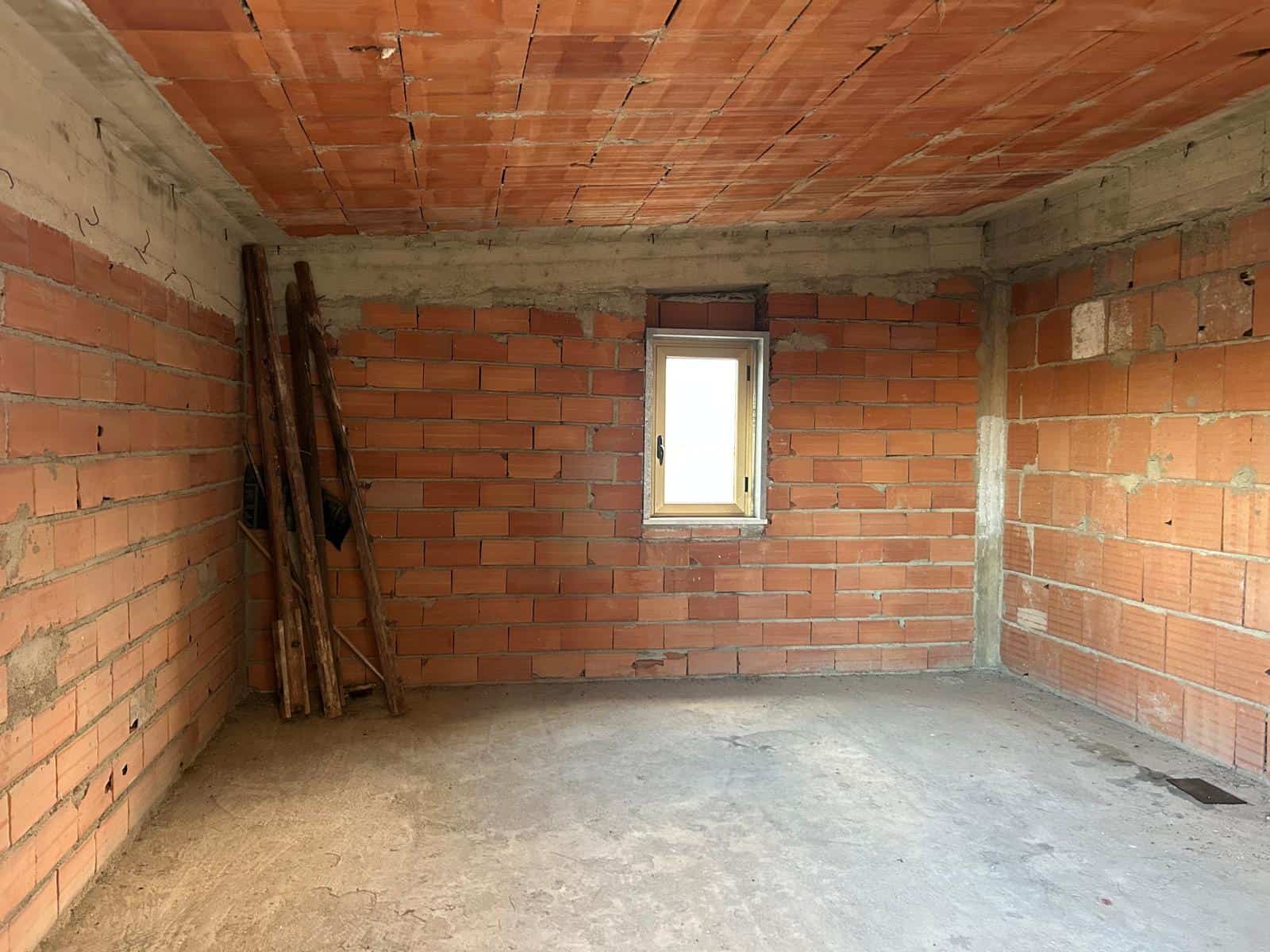 Interno di una stanza in costruzione con pareti in mattoni rossi, soffitto in legno e finestra piccola, pronto per finiture e arredi.