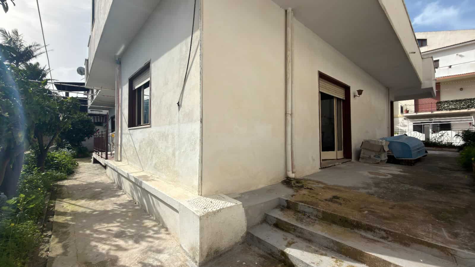 Ampia casa unifamiliare con ingresso su giardino e scala esterna, facciata in stucco bianco, finestra e porta d'ingresso in stile moderno, area di parcheggio e spazio esterno ben curato.