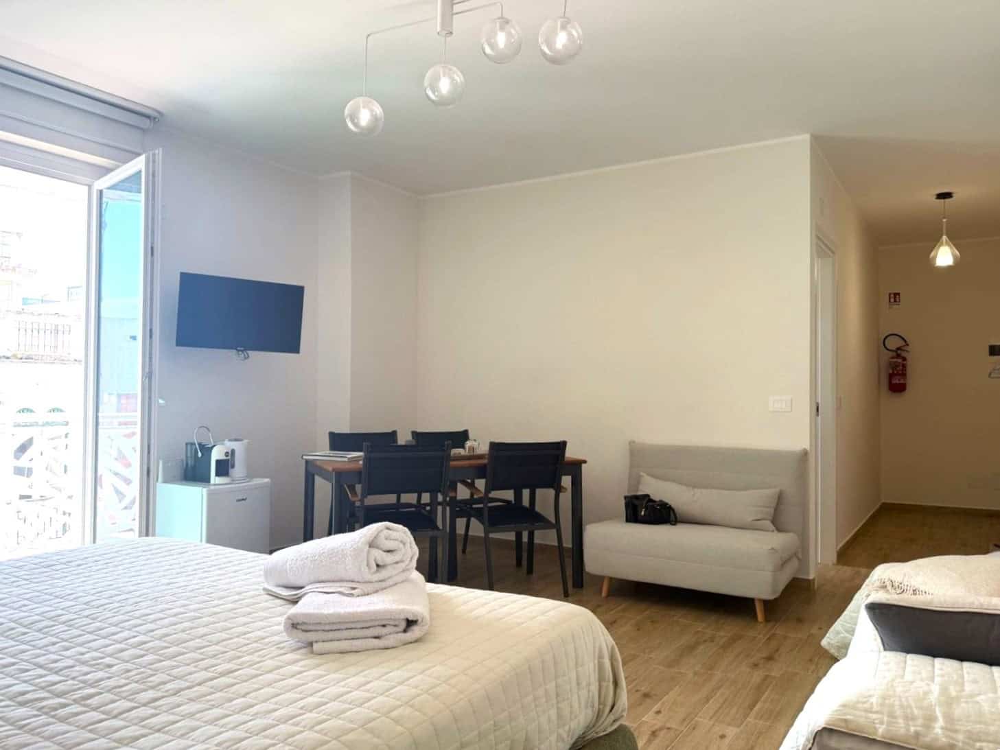 Appartamento moderno con soggiorno luminoso, zona pranzo e camera da letto con vista su balcone, arredato con stile minimalista, ideale per soggiorni confortevoli e rilassanti a NextCasa.