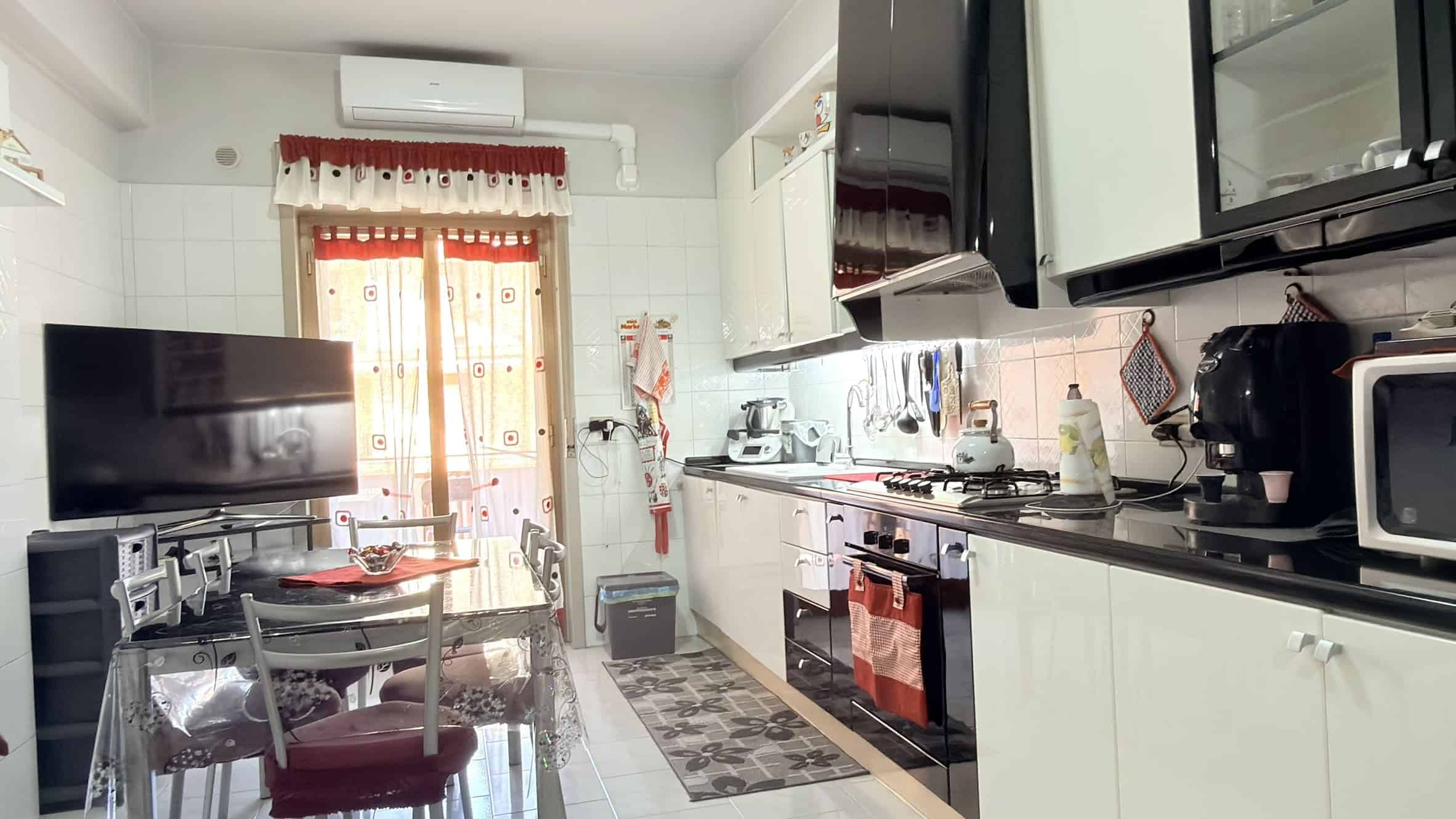 Pannello TV e cucina moderna in un ambiente luminoso con elettrodomestici bianchi e neri, dettagli pratici e funzionali, ideale per spazi abitativi confortevoli e ben organizzati.