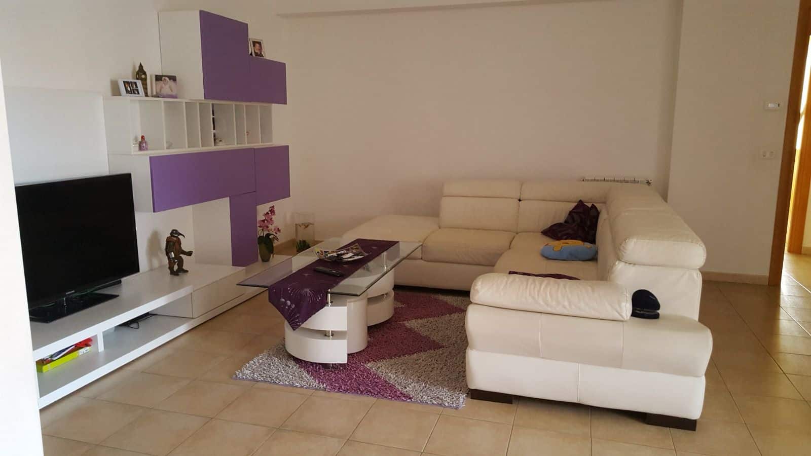 Divano angolare bianco in soggiorno con mobile TV moderno e decorazioni colorate, ambiente luminoso e accogliente, ideale per relax e intrattenimento domestico.