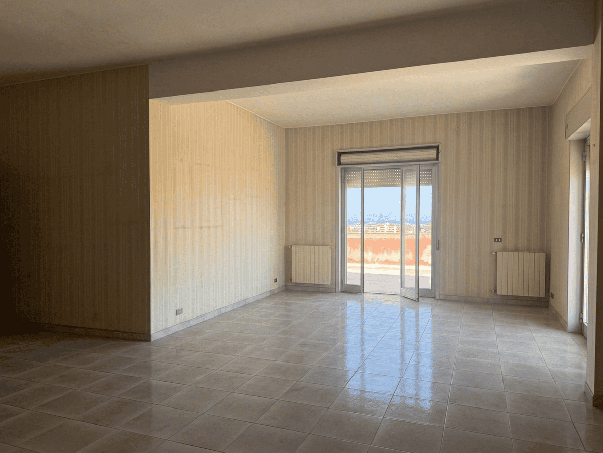 Ampio soggiorno luminoso con pareti in legno e grandi finestre che offrono vista panoramica sulla città e accesso a un balcone. Ideale per vivere e rilassarsi in ambienti moderni e accoglienti.