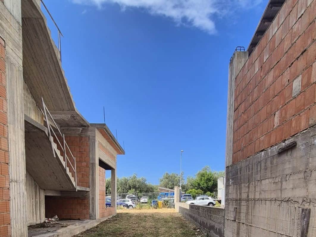 Cattura di un cantiere edilizio con strutture in mattoni e cemento, sotto un cielo sereno, che mostra un'area di costruzione in fase di sviluppo con veicoli parcheggiati sullo sfondo.