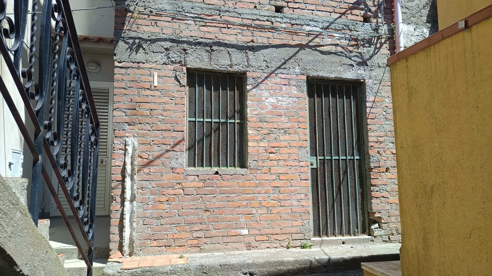 Scorcio di edificio residenziale con pareti in mattoni e inferriate alle finestre e alla porta, situato in un contesto urbano con elementi di sicurezza e struttura semplice.