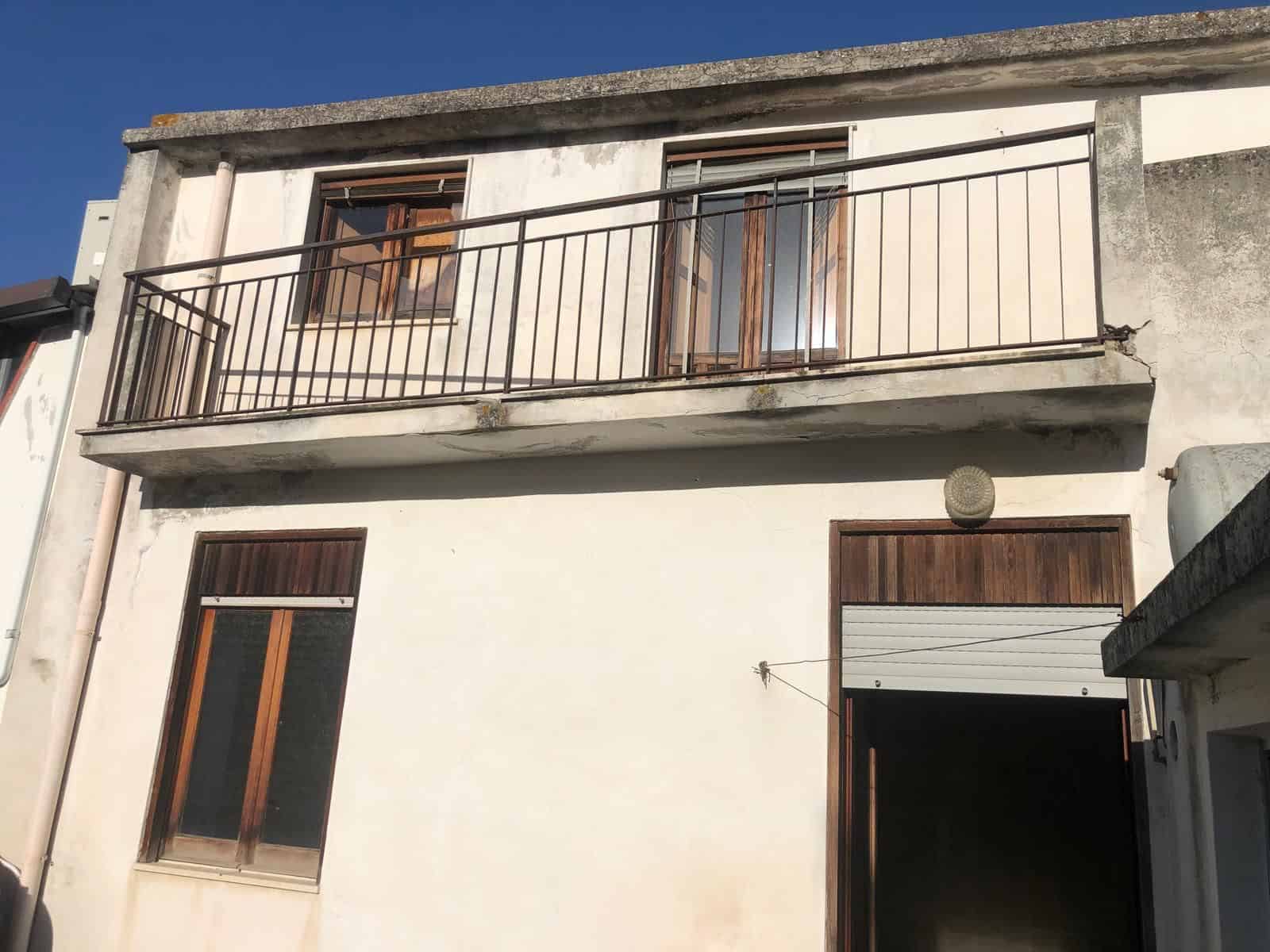 Barriera di sicurezza in metallo per balcone di una casa residenziale, con infissi in legno e pareti in cemento, in un contesto urbano.