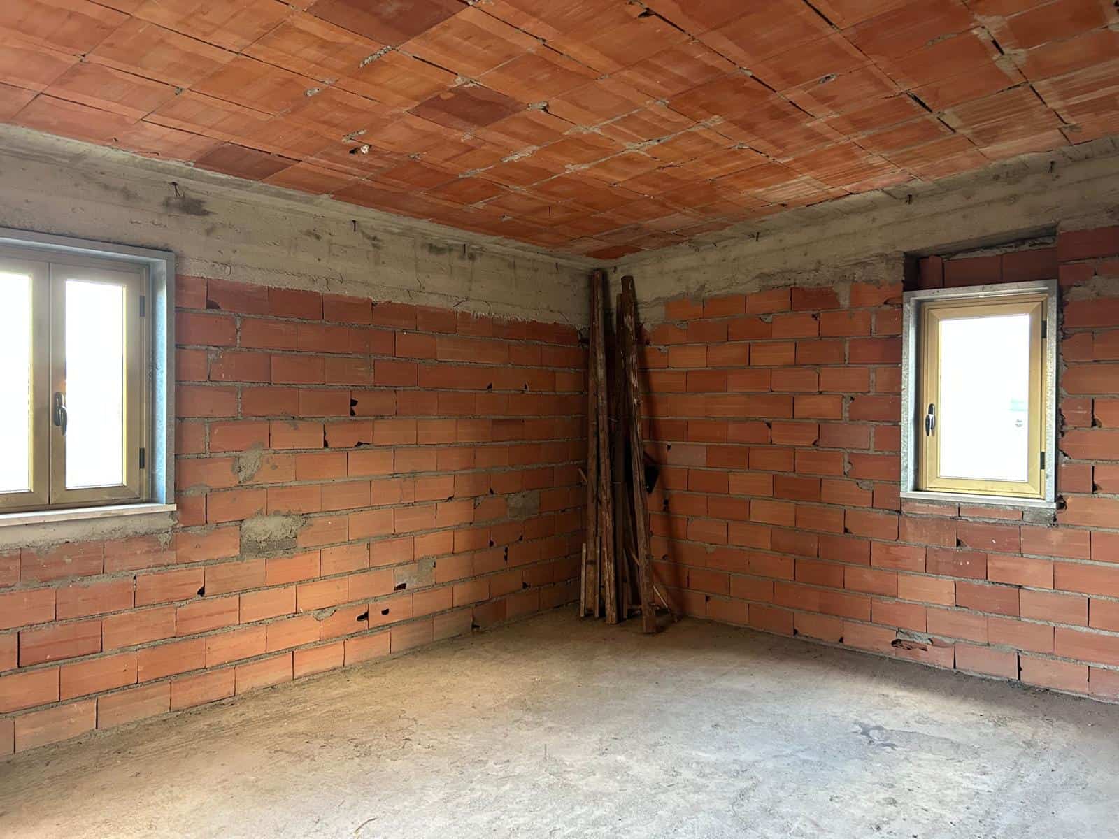 Interno di una stanza in costruzione con pareti in mattoni e finestre, pronto per finiture e rifiniture.