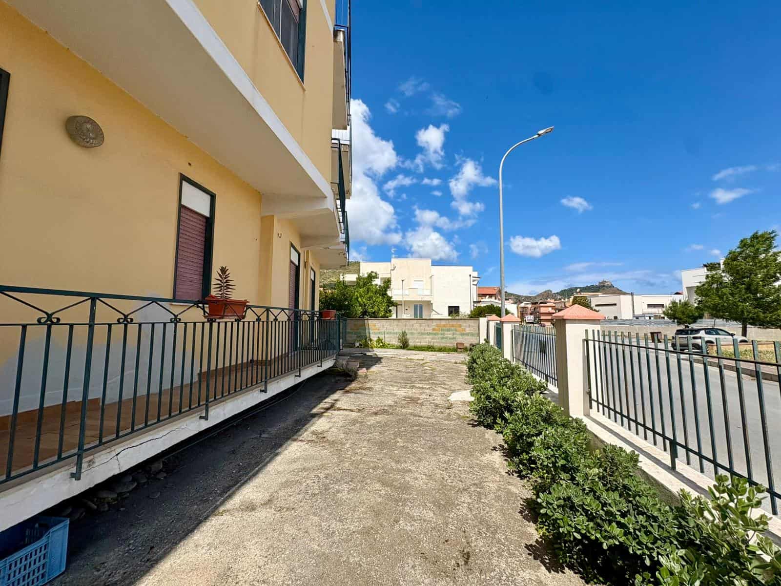 Spazio esterno di un appartamento con balcone e giardino, vista su strada e cielo sereno, edificio residenziale in zona urbana.
