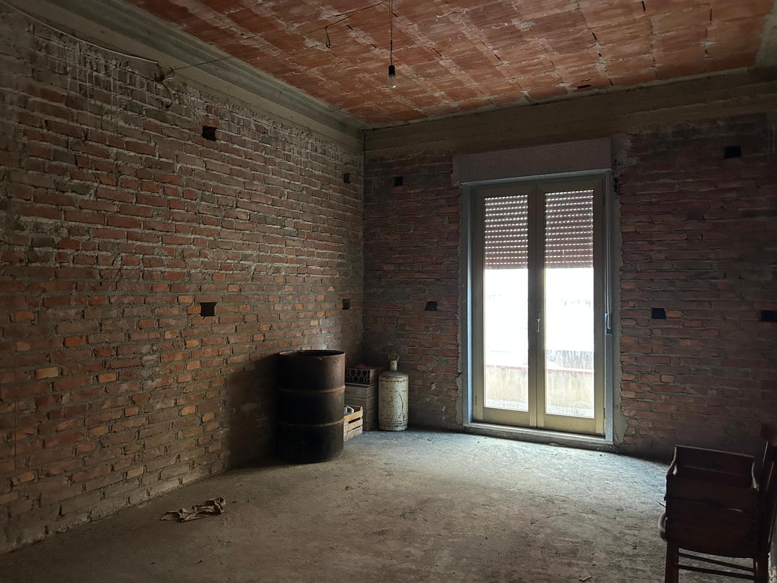 Appartamento in fase di ristrutturazione con pareti in mattoni a vista e grande finestra con balcone, pronto per essere personalizzato e arredato. Ideale per chi cerca un investimento immobiliare o un.