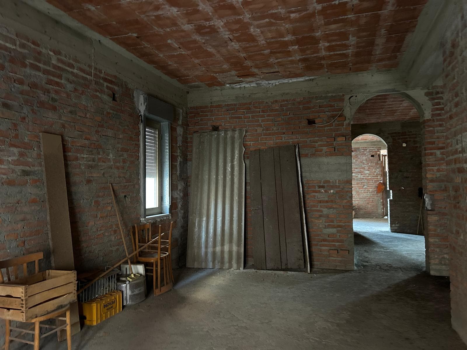 Immagine di un interno in fase di ristrutturazione con pareti in mattoni a vista, materiali edili e un arco che conduce ad un'altra stanza, ambiente luminoso e in costruzione.