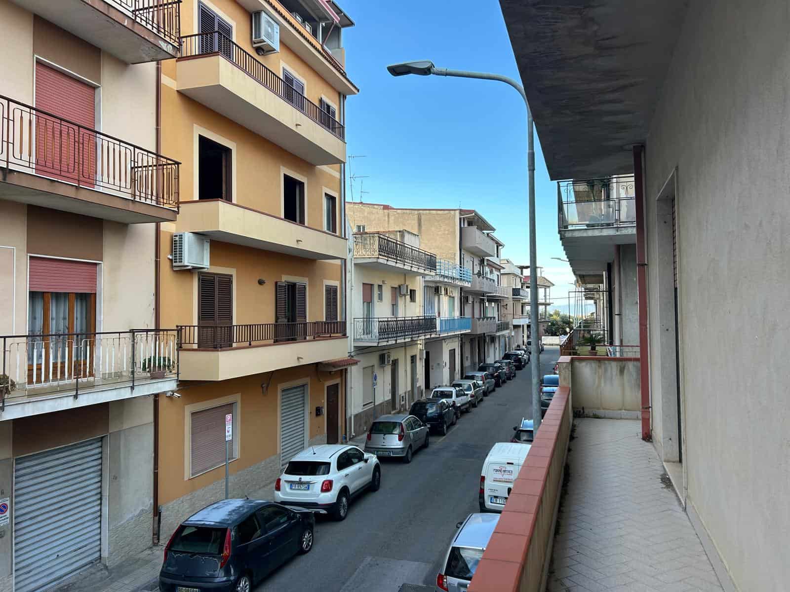 Vista di un quartiere residenziale con edifici a più piani e auto parcheggiate lungo la strada, in una giornata soleggiata.