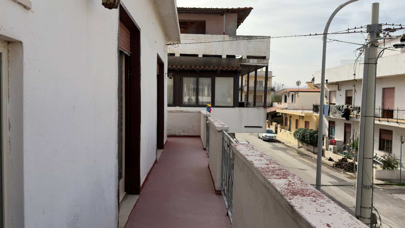 Balcone di un appartamento in zona residenziale con vista sulla strada e edifici circostanti, in Italia.