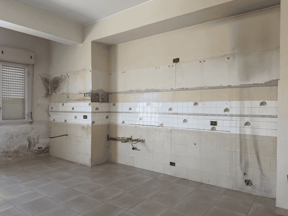 Lavagna da cucina con pareti danneggiate e piastrelle rotte, pronto per ristrutturazione, in un appartamento in attesa di restauro.