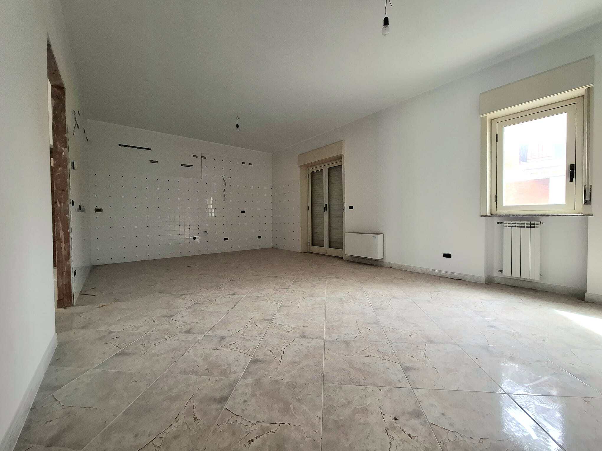 Ampia stanza luminosa in fase di ristrutturazione con pareti bianche e grandi finestre, ideale per appartamenti moderni e personalizzabili.