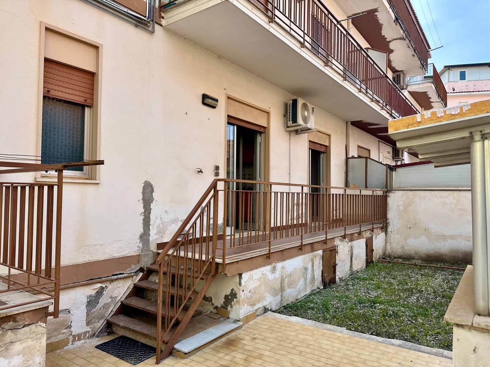 Balcone di un edificio residenziale con ringhiera in metallo, pareti esterne con segni di usura e un'unità di condizionamento, in un contesto urbano.