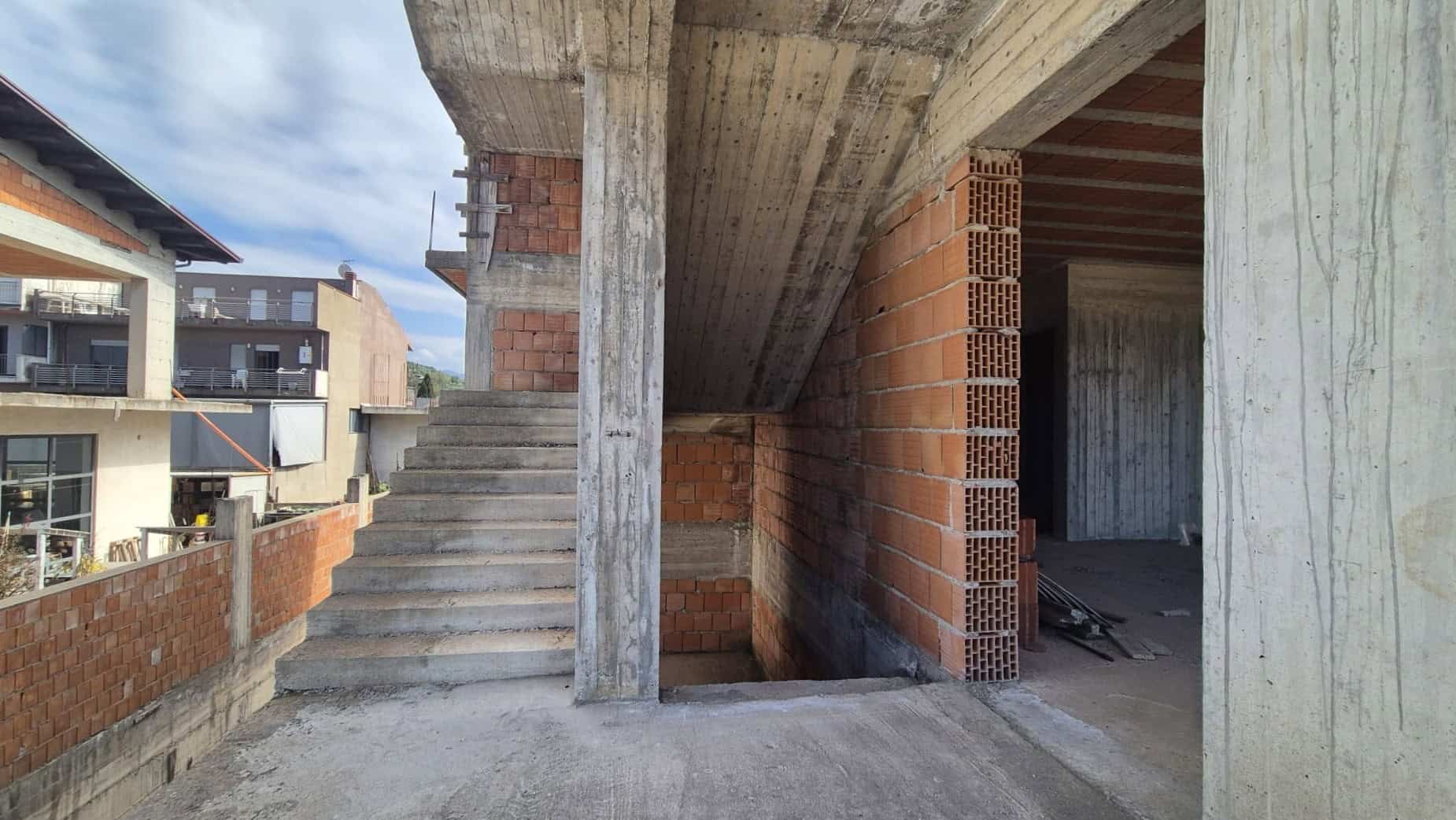 Scorcio di un edificio in costruzione con struttura in cemento e mattoni rossi, pronto per essere completato, rappresentando un esempio di progetto immobiliare in fase di sviluppo.