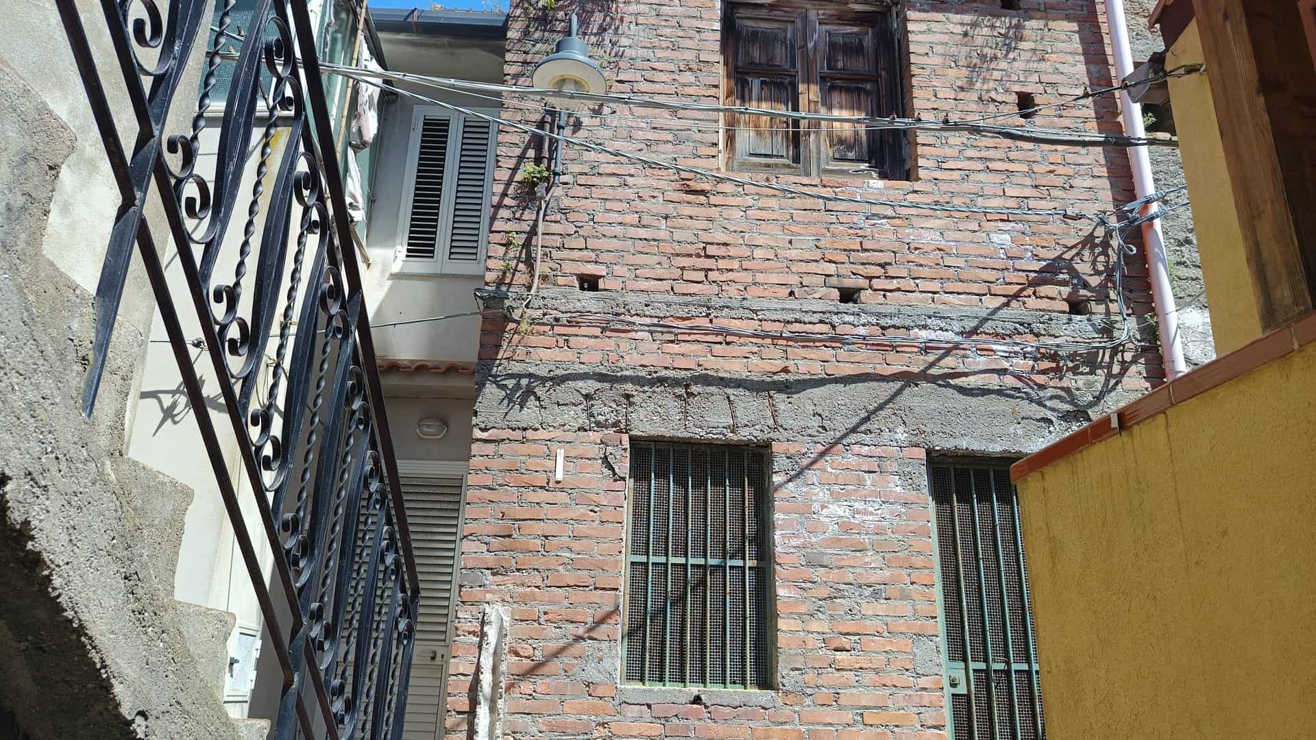 Facciata di un edificio in mattoni con finestre con grate e cavi elettrici, vista da strada stretta, in un contesto urbano.