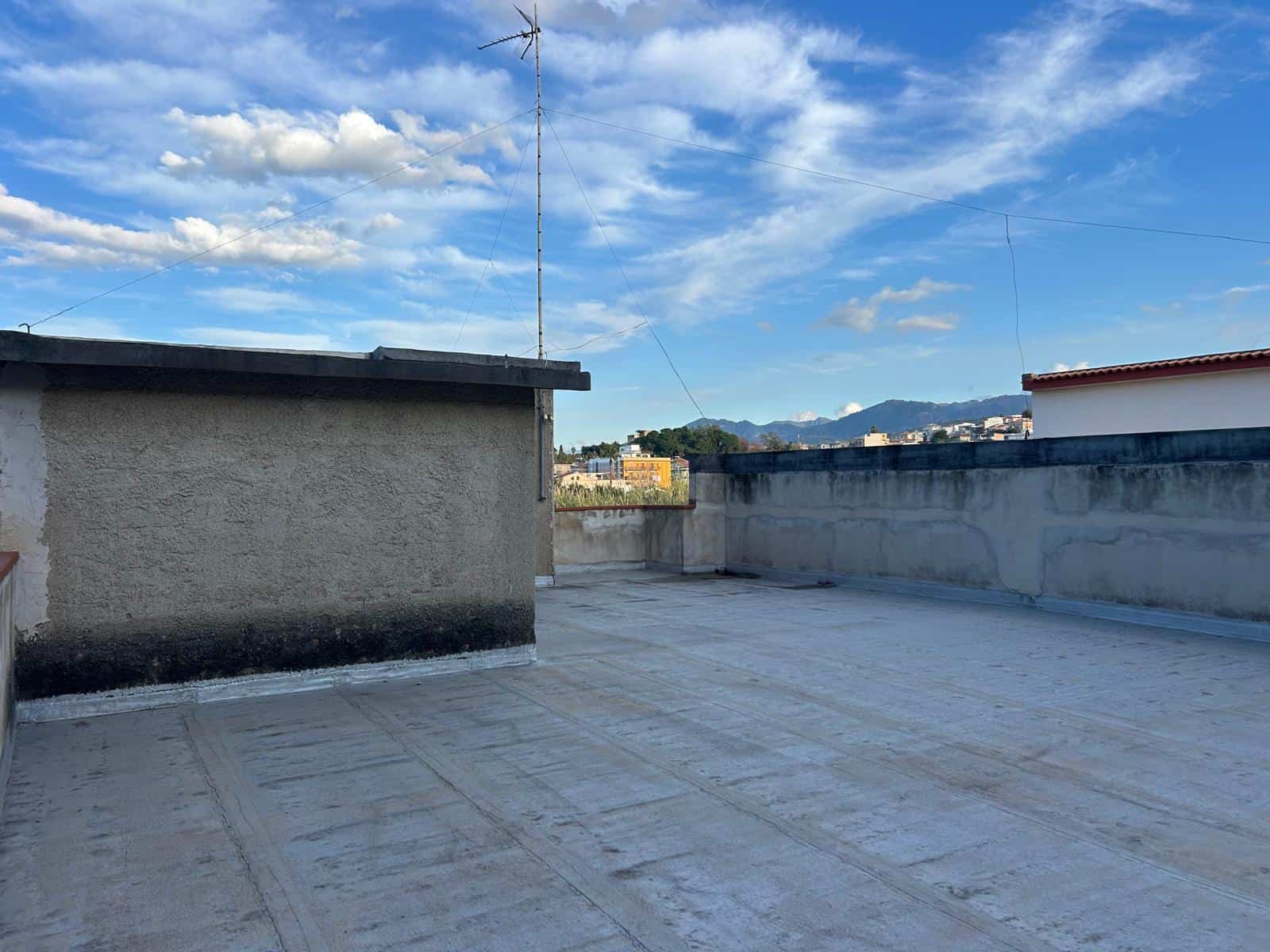 Il tetto di un edificio con vista sul cielo azzurro e nuvole bianche, con montagne sullo sfondo, in un ambiente urbano.