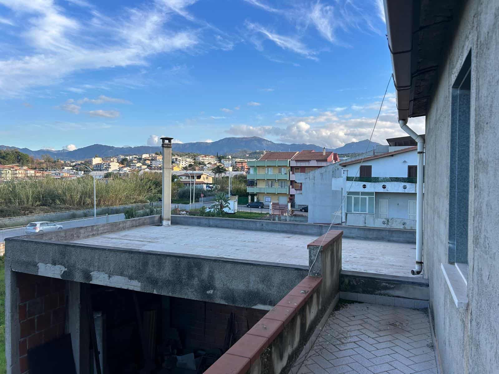 Balcone di un appartamento con vista panoramica sulle montagne e sulla città, in un contesto residenziale con edifici moderni e cielo sereno.