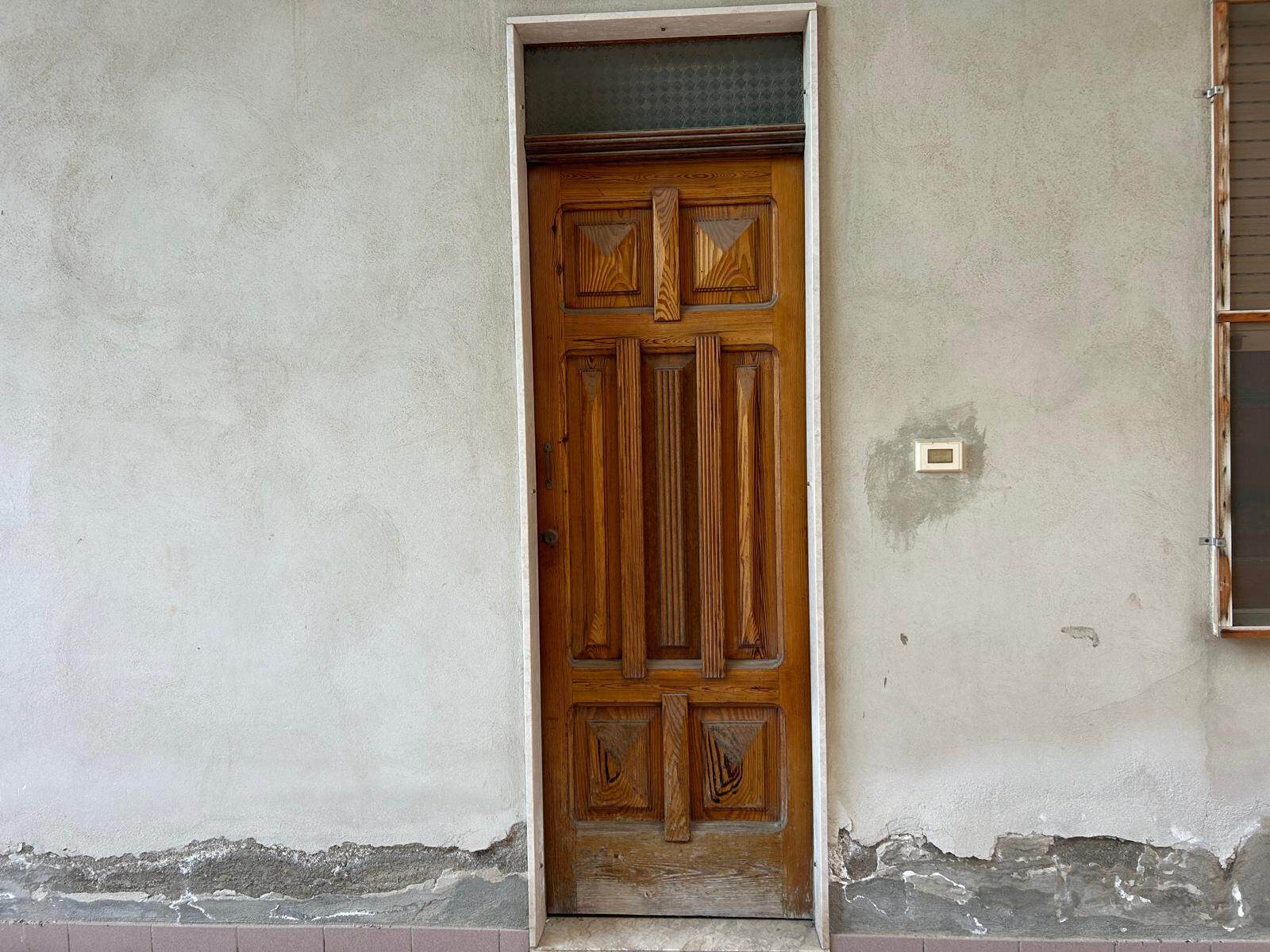 Il portone in legno su una parete esterna di una casa, con dettagli artigianali e finiture rustiche, rappresenta un elemento di ingresso tradizionale e accogliente.