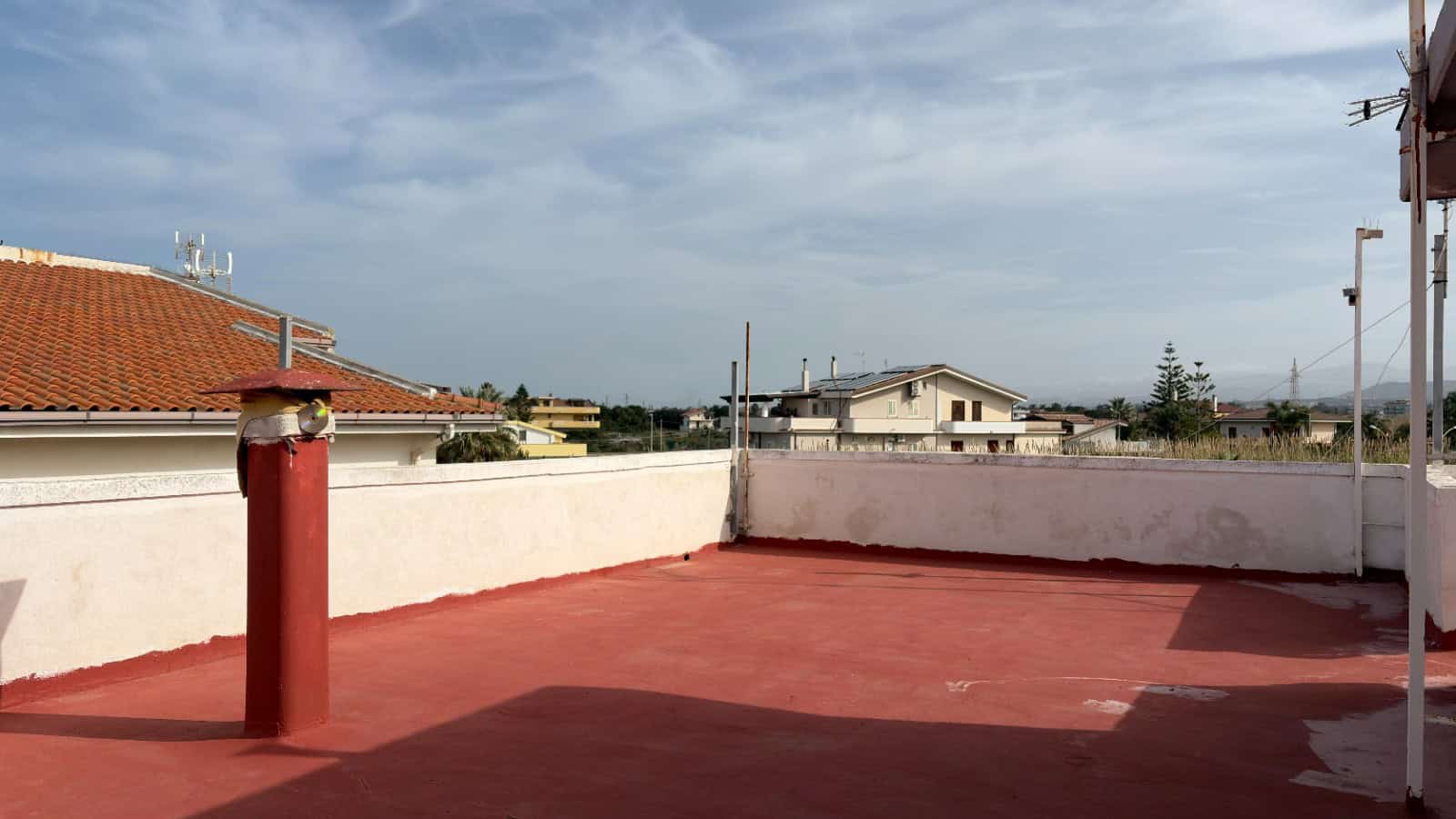 Aggiunta di un'antenna e di un camino sul tetto di un edificio residenziale con vista sul cielo e sulle case circostanti, in Italia.
