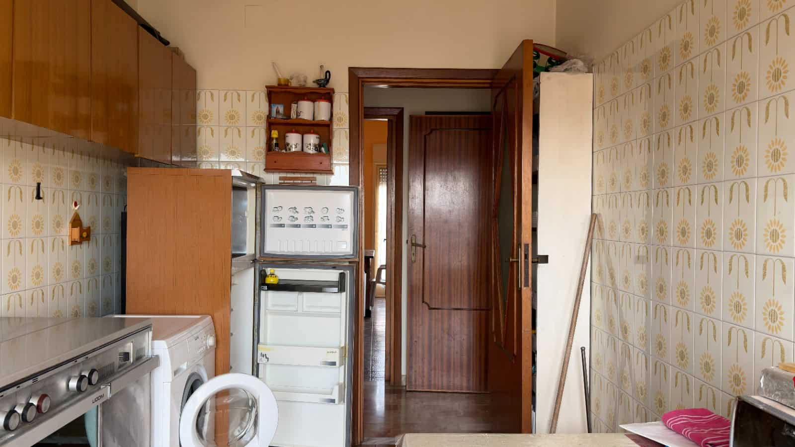 Ampio spazio in cucina con elettrodomestici moderni e armadietti in legno, pareti decorate con piastrelle vintage, porta in legno che conduce a un'altra stanza, ambiente funzionale e accogliente.