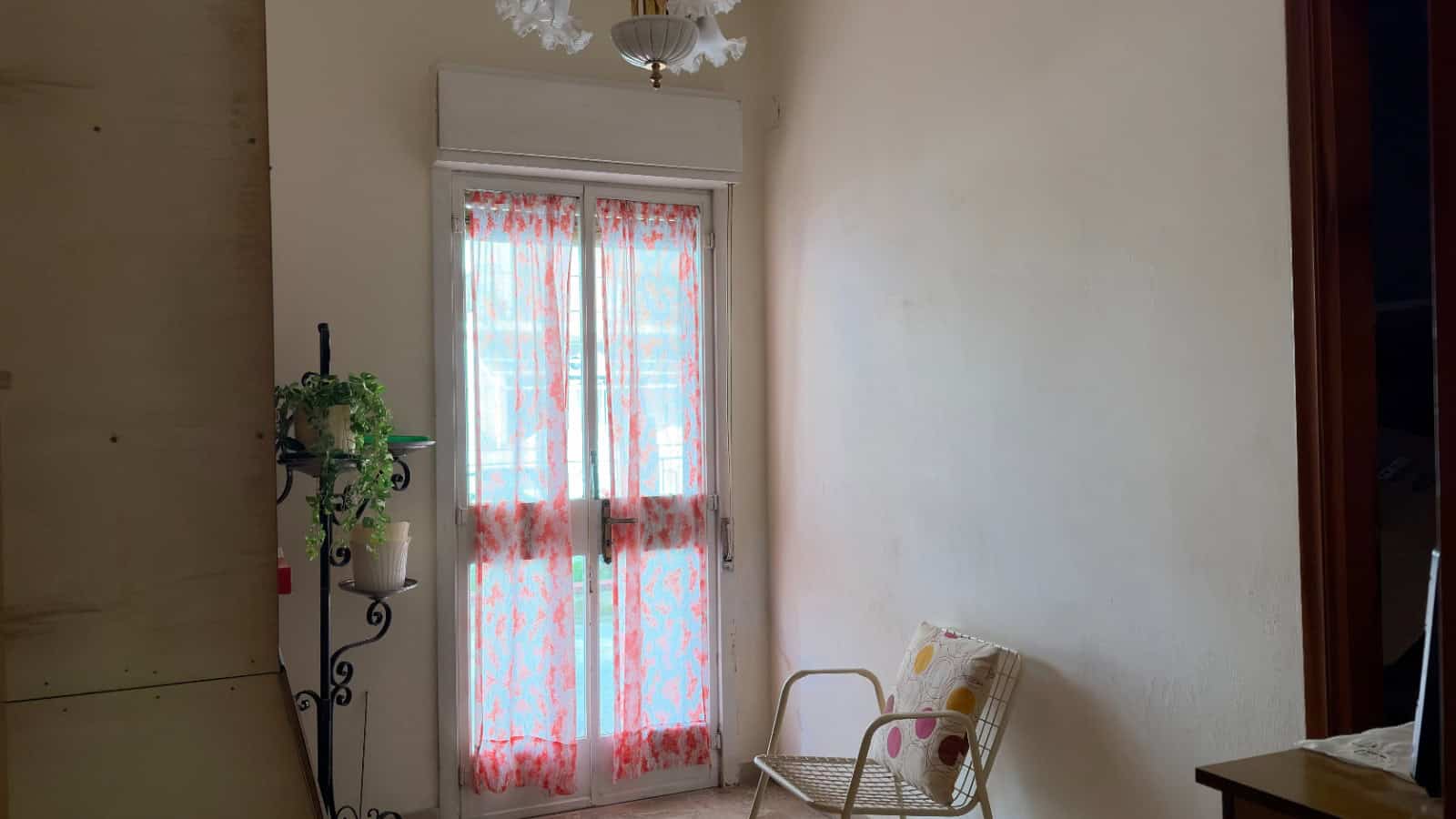 Porte finestra con tende leggere e decorazioni floreali, illuminata da luce naturale, in un ambiente domestico accogliente e luminoso.
