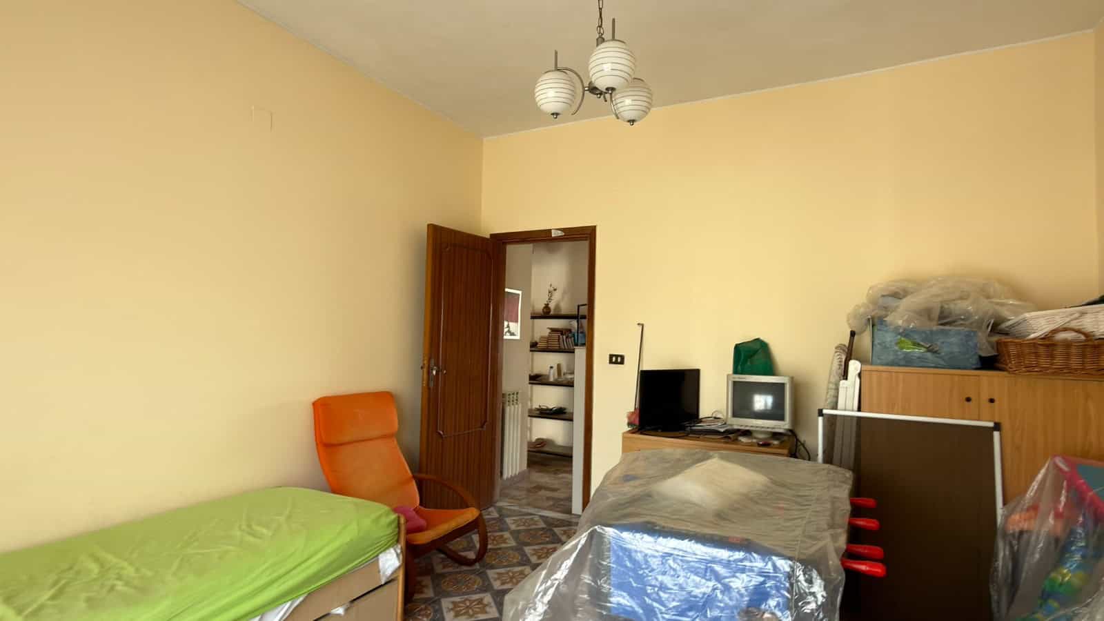 Ampio soggiorno con scrivania, sedia ergonomica e armadio, ambiente luminoso e accogliente, ideale per lavoro o relax, con pareti color crema e arredi pratici.