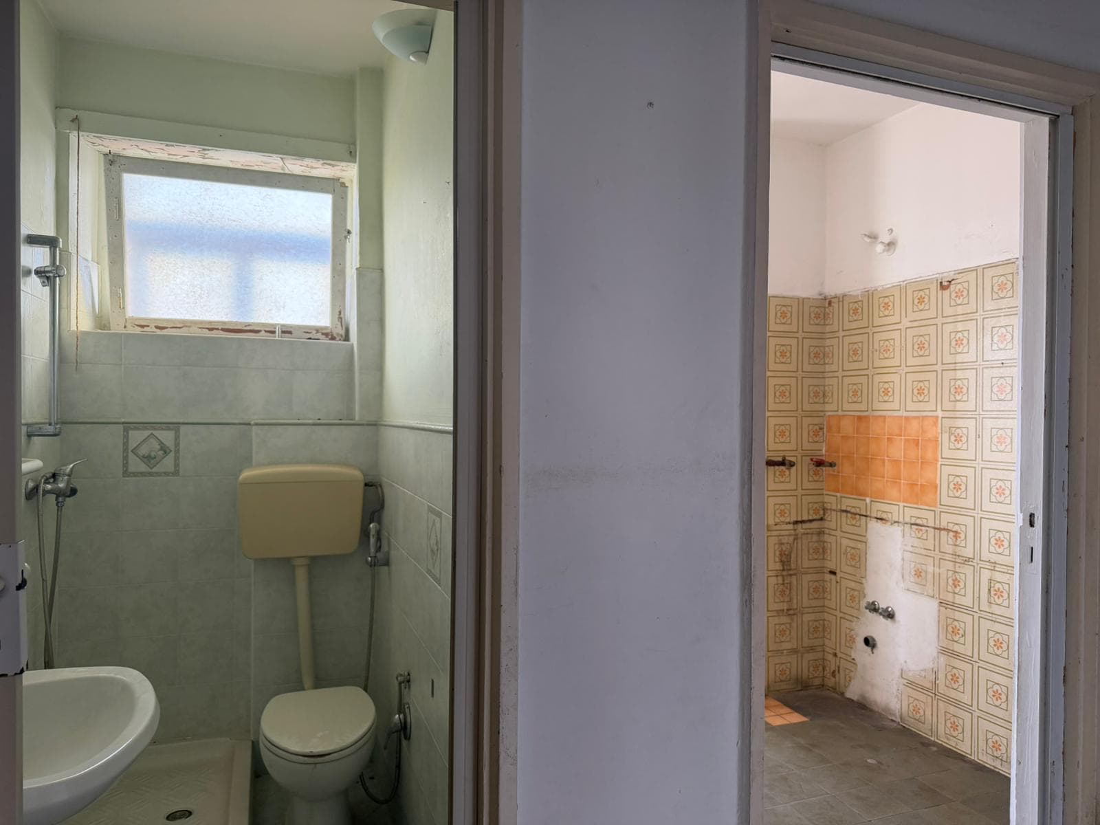 Bagno con finestra, sanitari e piastrelle vecchie, ambiente di una casa da ristrutturare, vista da una porta aperta, illuminato dalla luce naturale, stile semplice e funzionale.