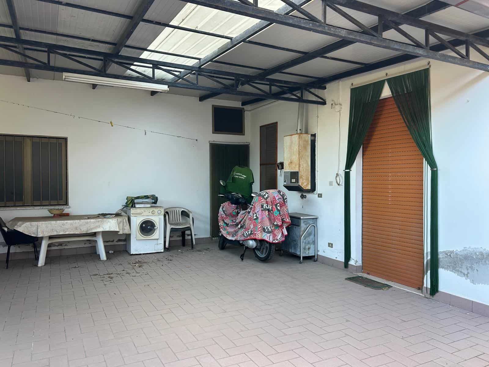 Ampio spazio esterno coperto con pavimento in piastrelle, area lavanderia con lavatrice e stendibiancheria, e ingresso con porta avvolgibile in legno, ideale per attività all'aperto e relax.