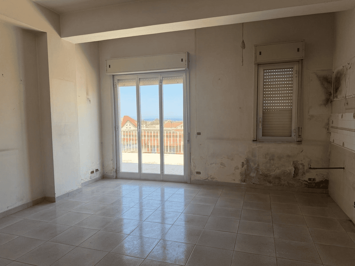 Aggiunta di un'immagine di un interno di appartamento in fase di ristrutturazione con grandi finestre e vista sulla città, pronto per essere arredato e personalizzato.